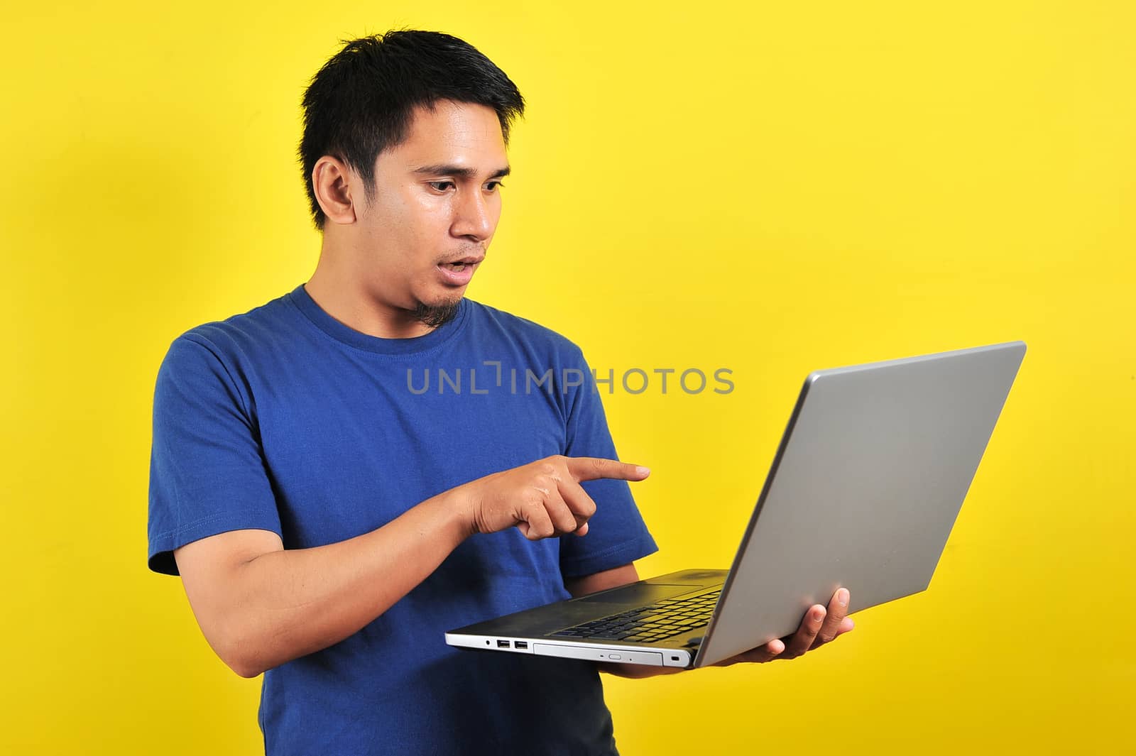 Asian man shocked what he see in the laptop, isolated on yellow background