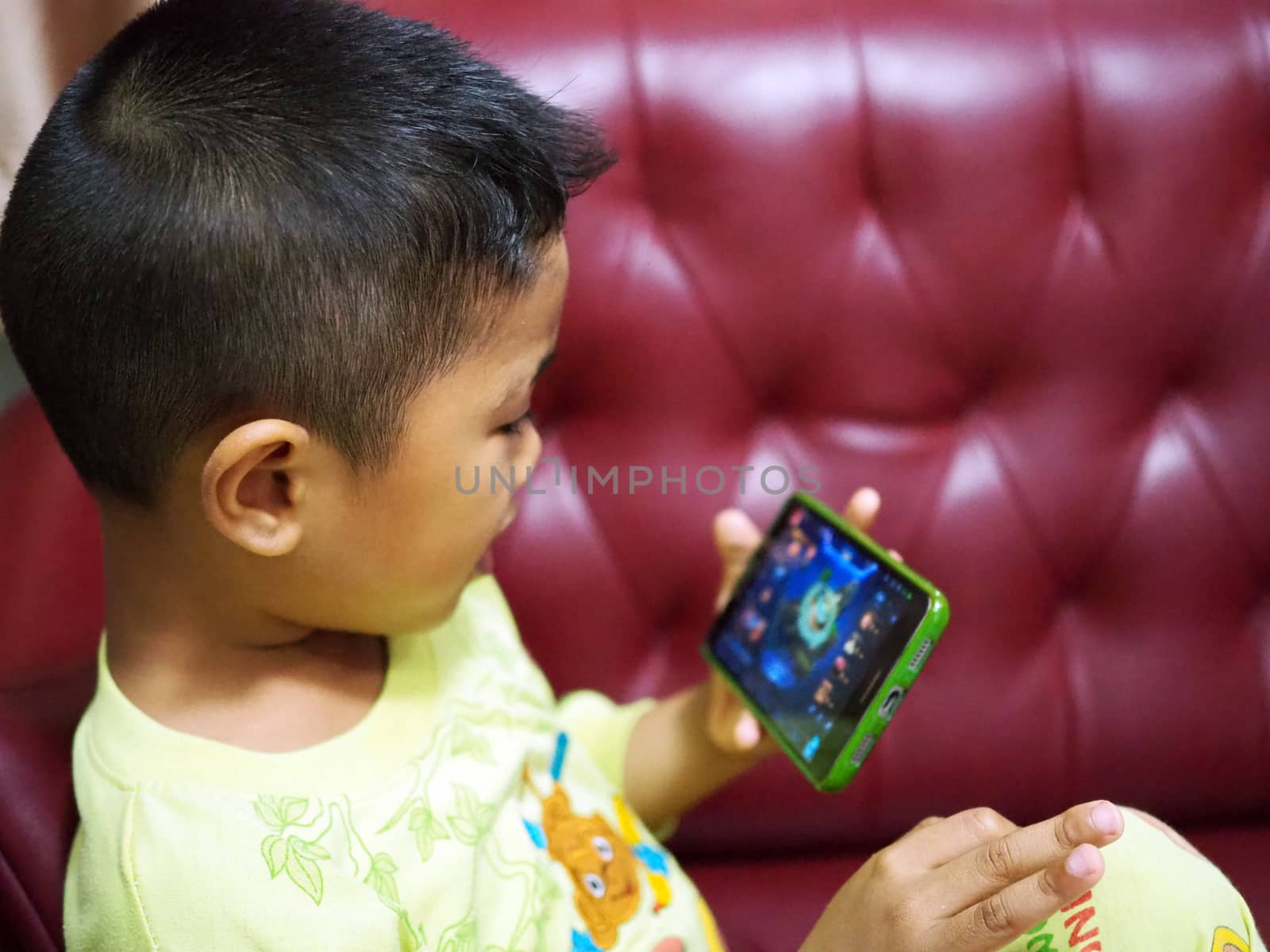 The boy is playing games in the mobile phone. On the red sofa intently. Phone blurred screen.