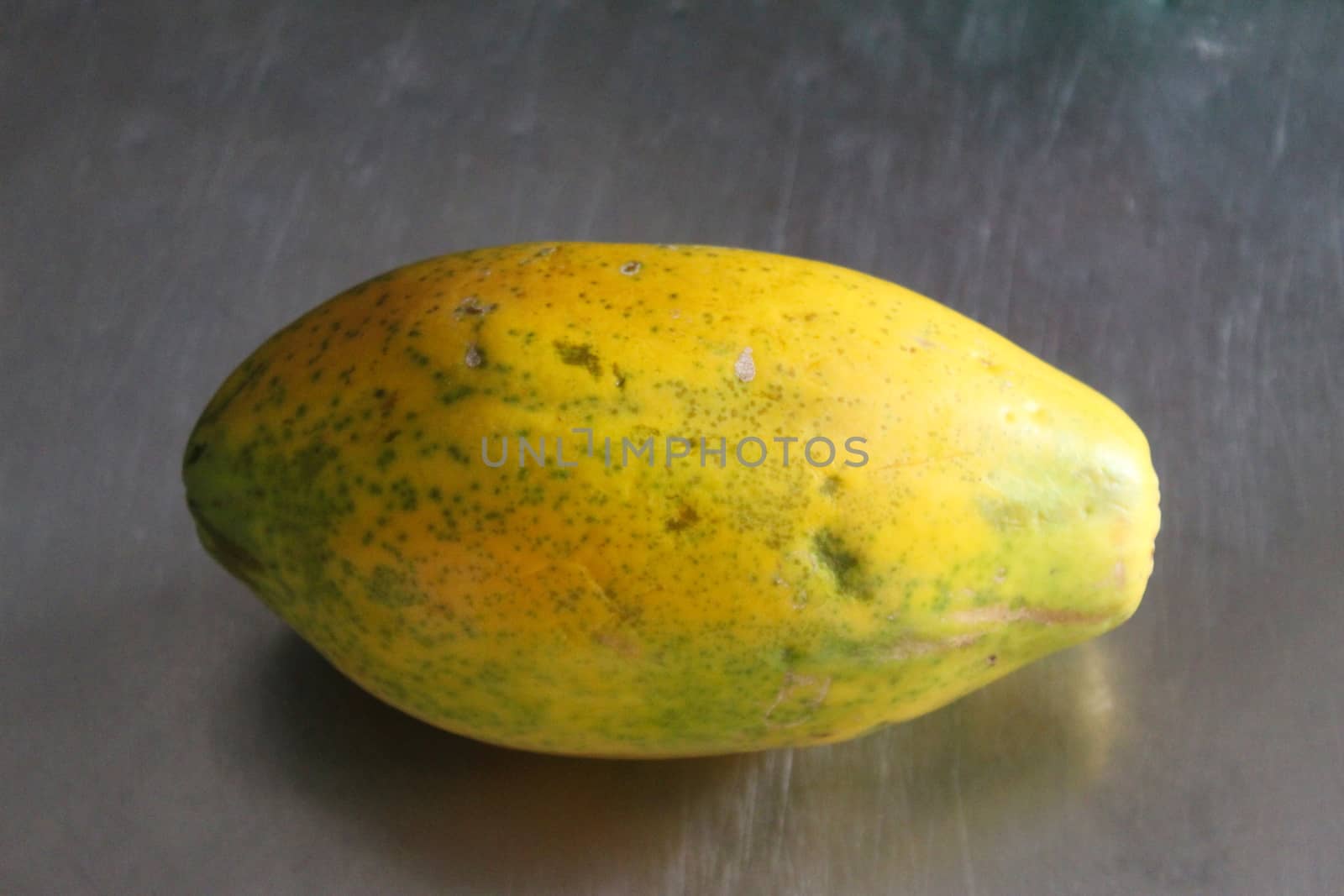 Whole papaya fruit on the kitchen table. Gray metal background.