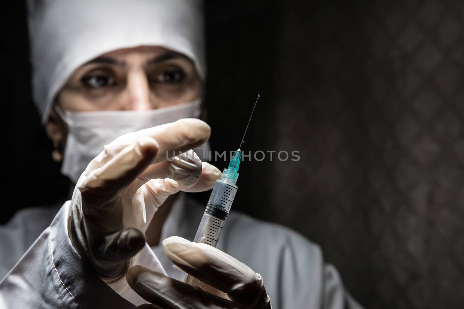 Health medical concept. Serious female doctor in medical mask holding syringe. Health worker dials the vaccine into a syringe on dark background.