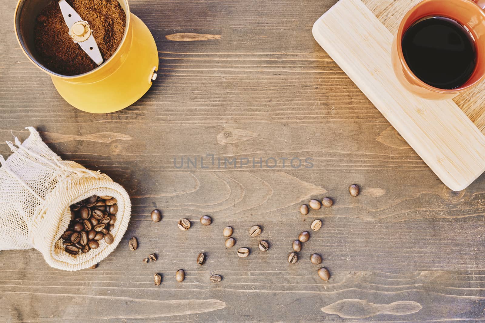 Coffee cup, coffee beans in a bag and a grinder with ground coffee on a wooden table by Daniel_Mato