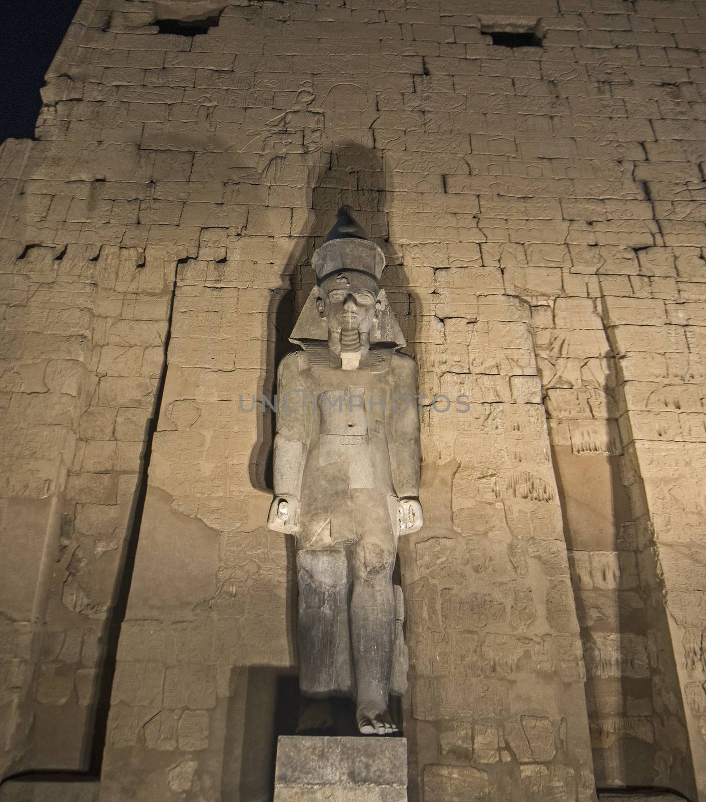 Wall with hieroglyphic carvings and statue of Ramses II in ancient egyptian Luxor Temple at night