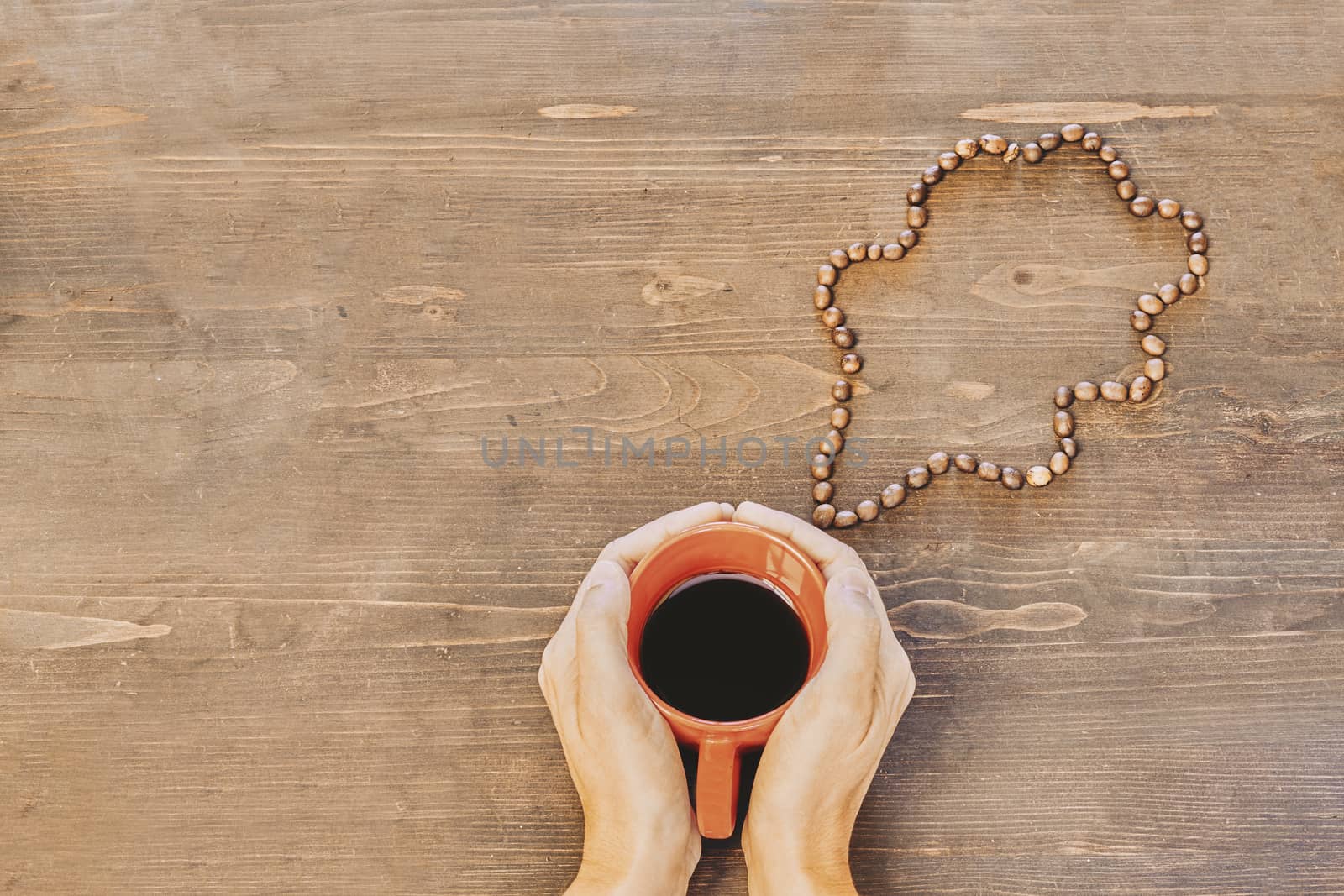 Hands holding a red coffee cup on a wooden table with a cloud made of coffee beans by Daniel_Mato