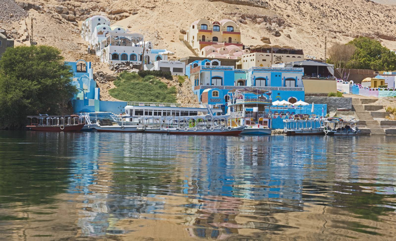 View from river Nile in Aswan Egypt to riverbank through rural countryside landscape with traditional Nubian village houses on shore and reflection