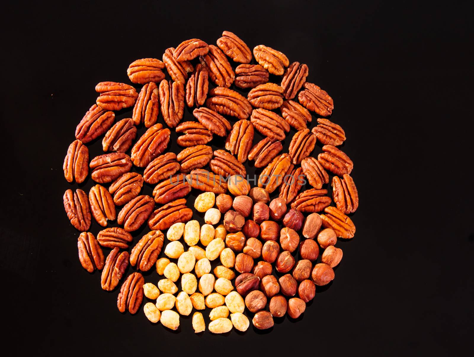 Assorted nuts (Pecan, Hazelnuts and Roasted Salted Peanuts) in a circle form on a black background