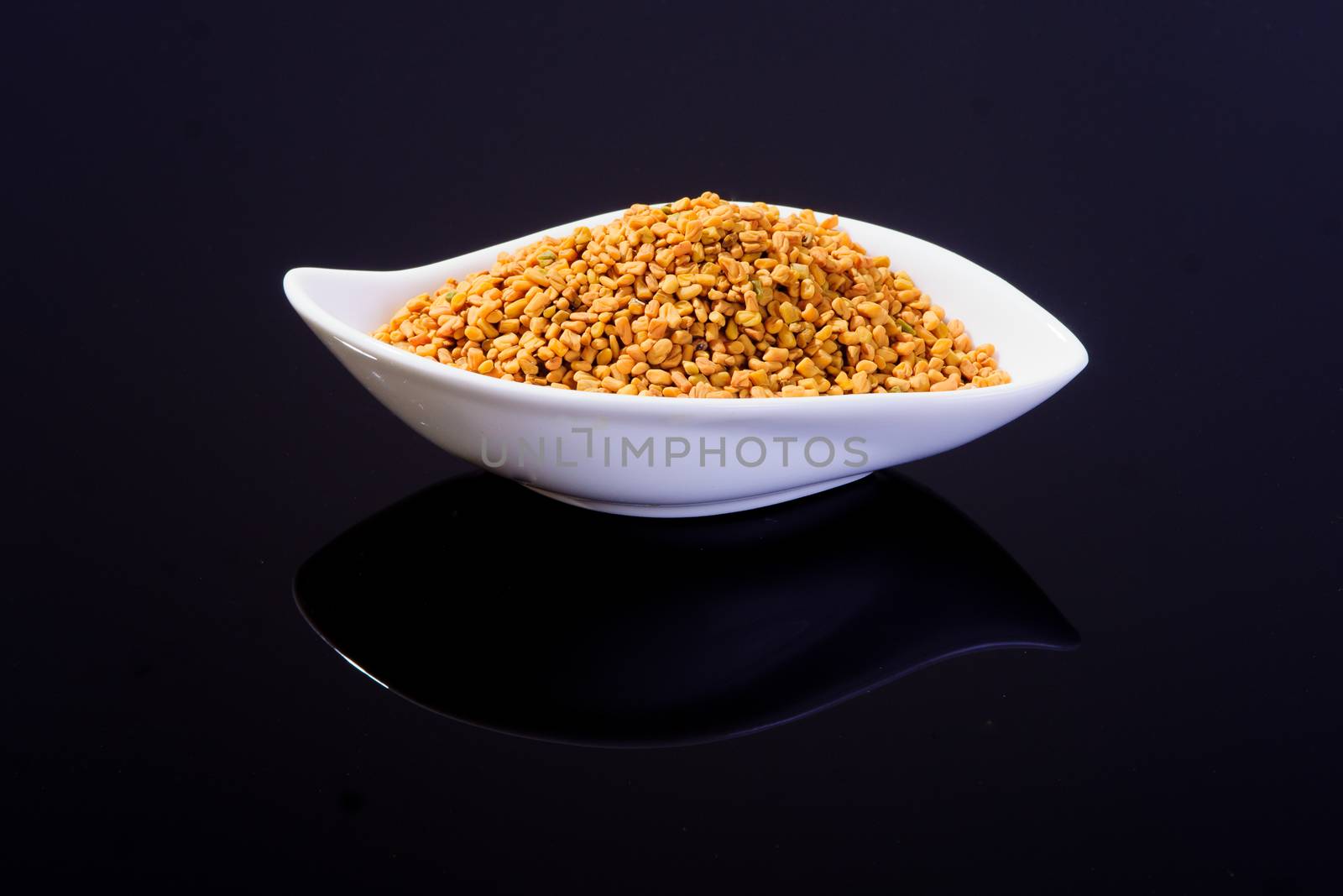 Fenugreek seeds in a white bowl on black surface