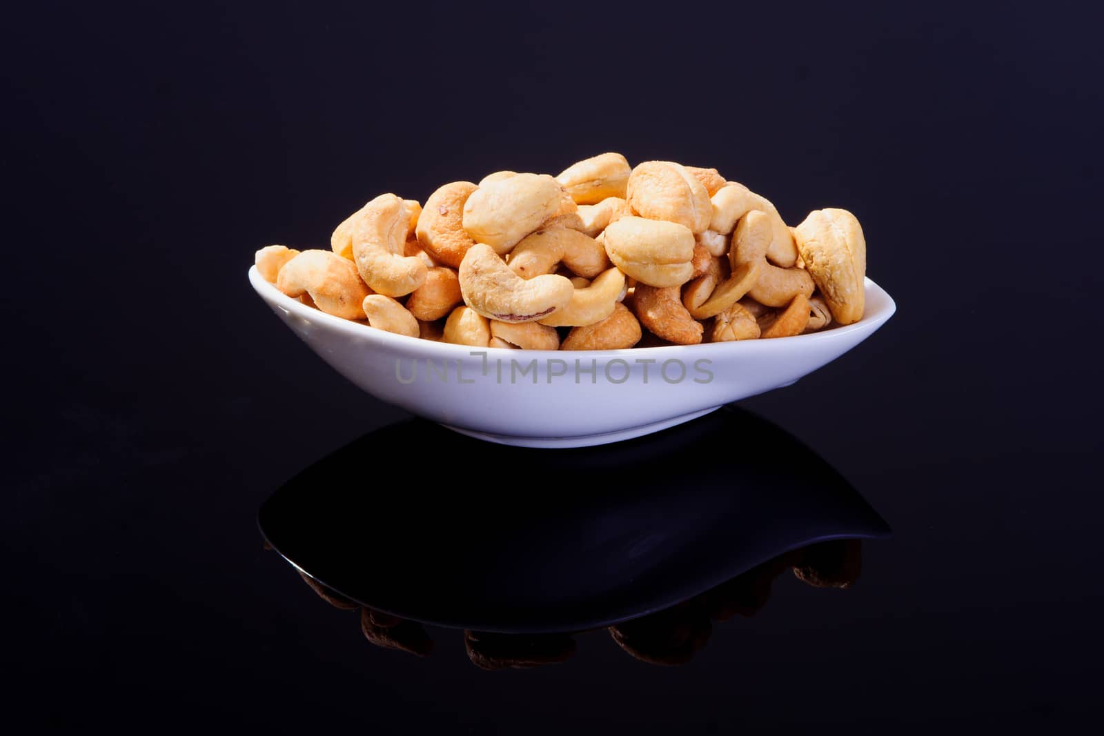 Salted Cashew Nuts in a white plate on a black background