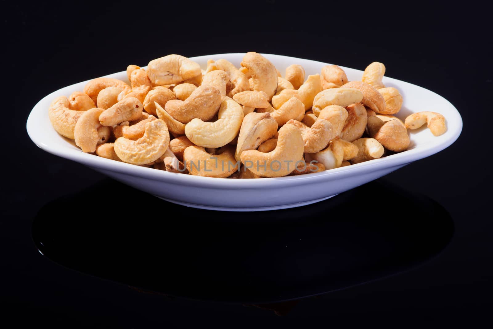 Salted Cashew Nuts in a white plate on a black background