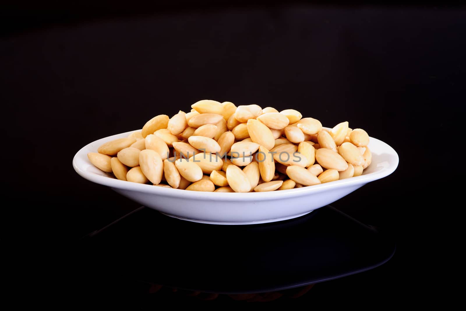 Blanched Almonds in a white plate on a black background