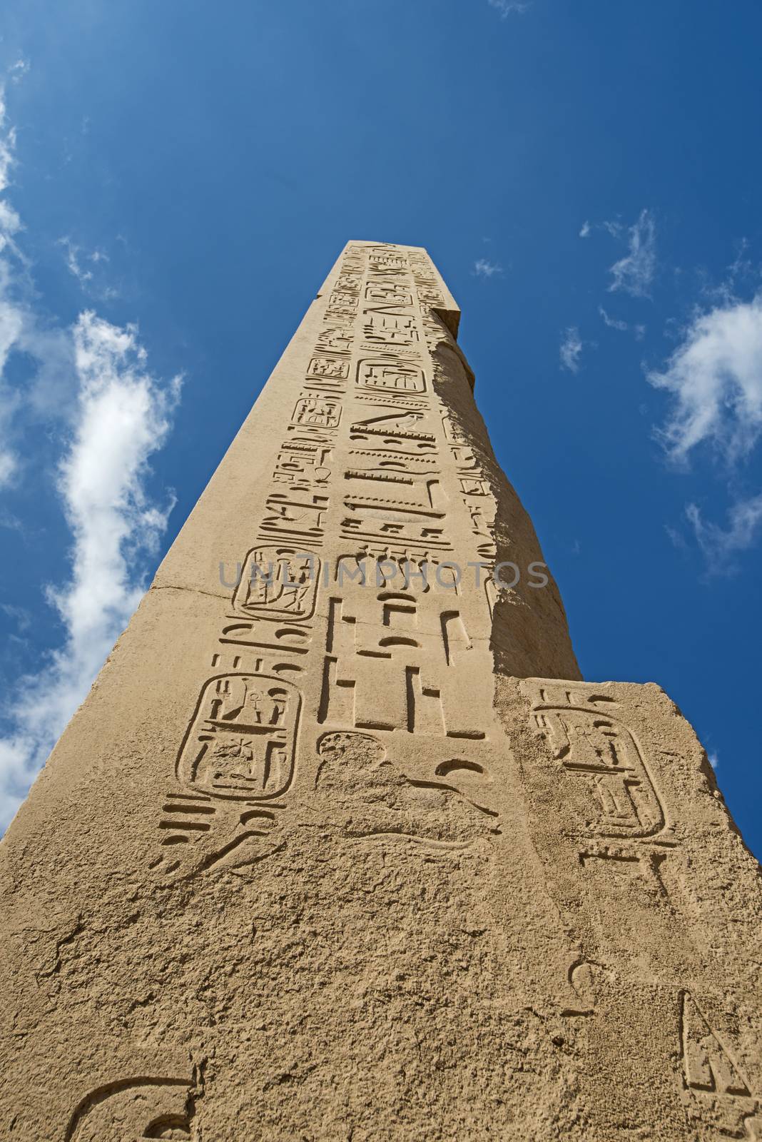 Large tall ancient egyptian obelisk at the temple of Karnak in Luxor with hieroglyphic carvings on blue sky background