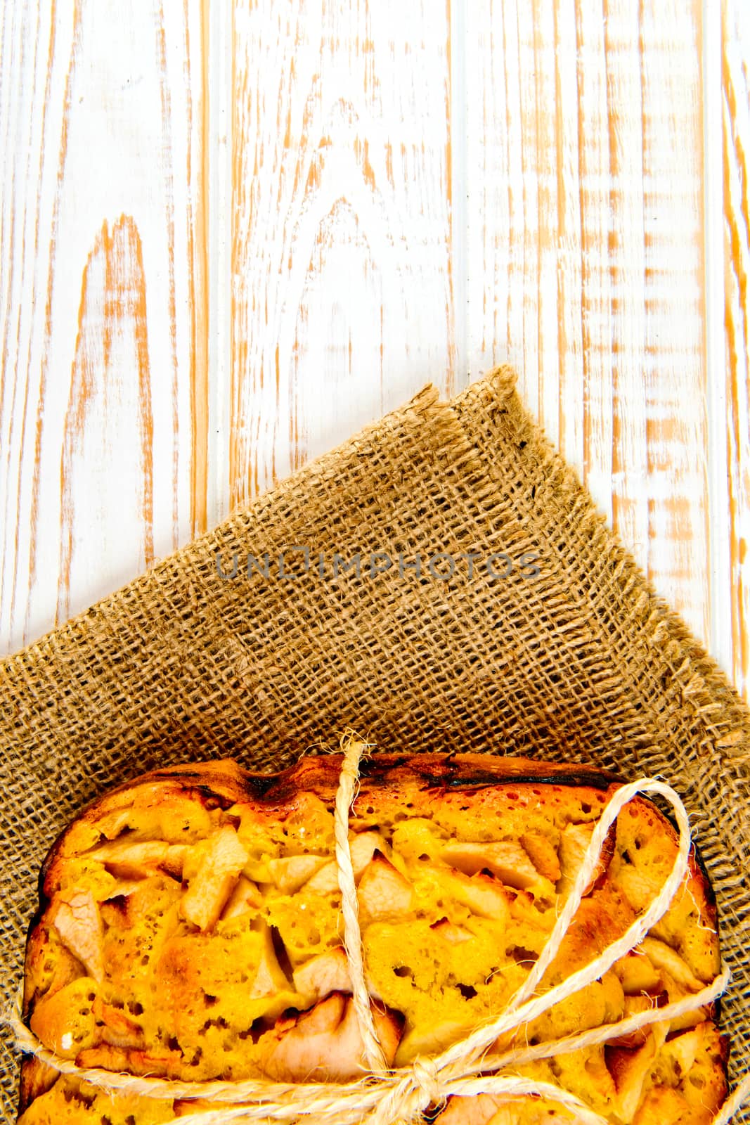 Fresh bakery. Top view of baked pie with apples on sackcloth on a white wooden background. Rustic style.
