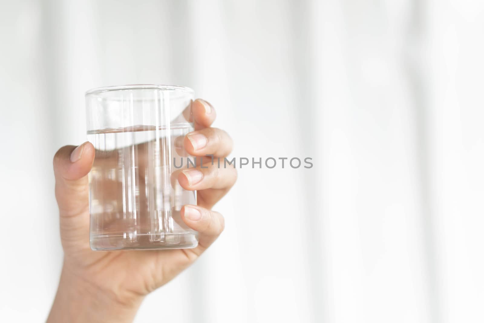 Closeup woman hand holding a glass of pure water for dink with grey background, Health care concept