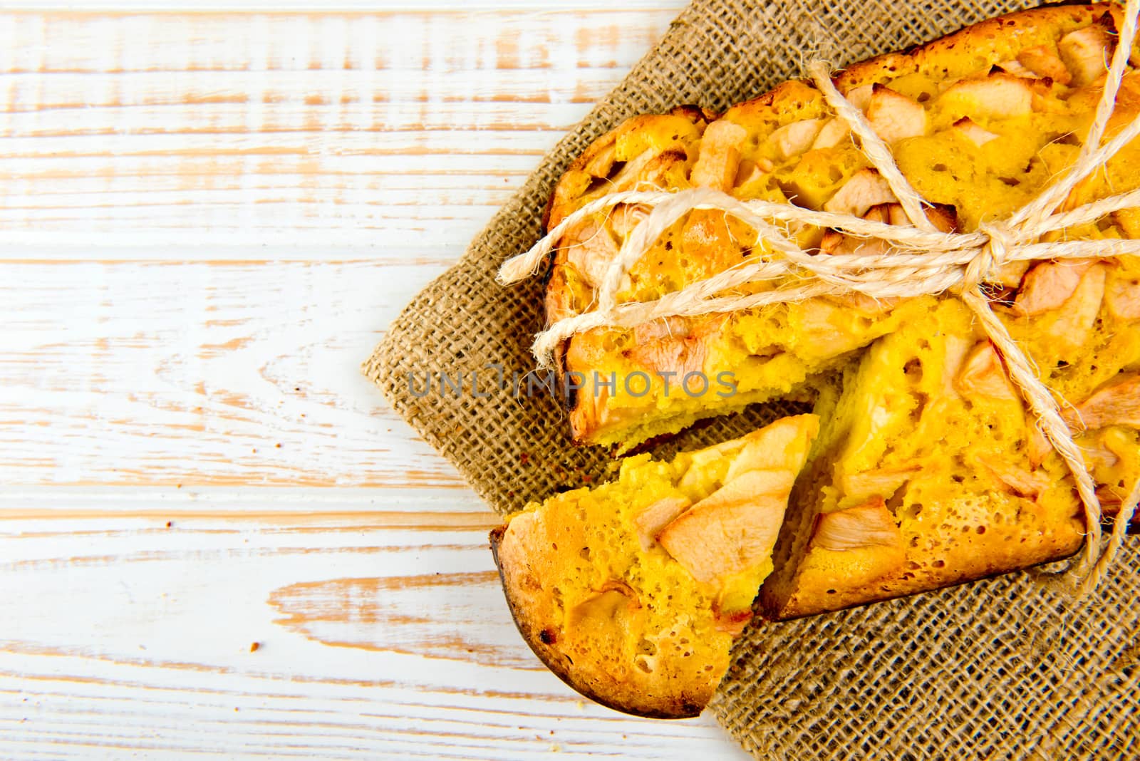 Fresh bakery. Top view of baked pie with apples on sackcloth on a white wooden background. Rustic style.