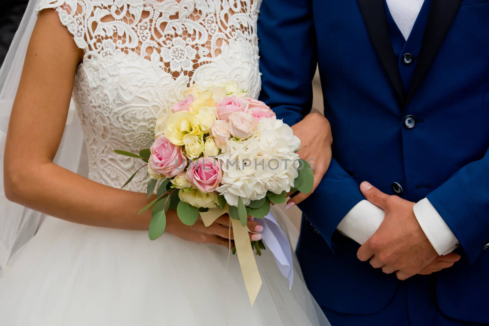 The bride and groom stand with their hands together. The bride's bouquet.