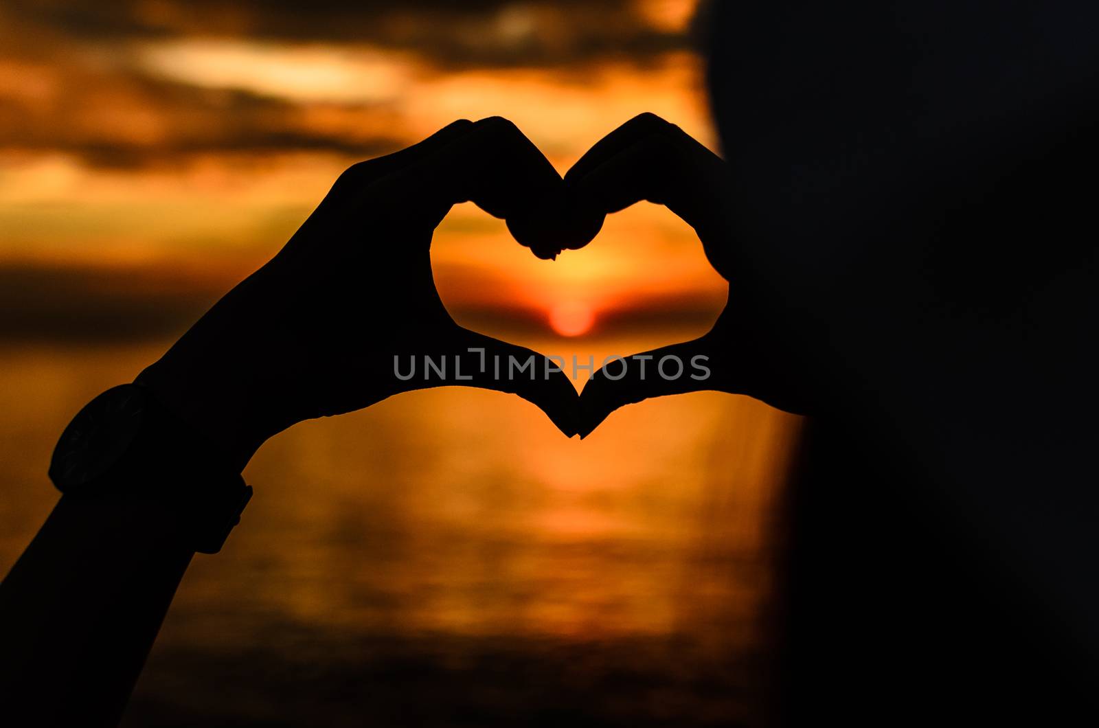 Sunset of love in the heart hand on the sea with silhouette.