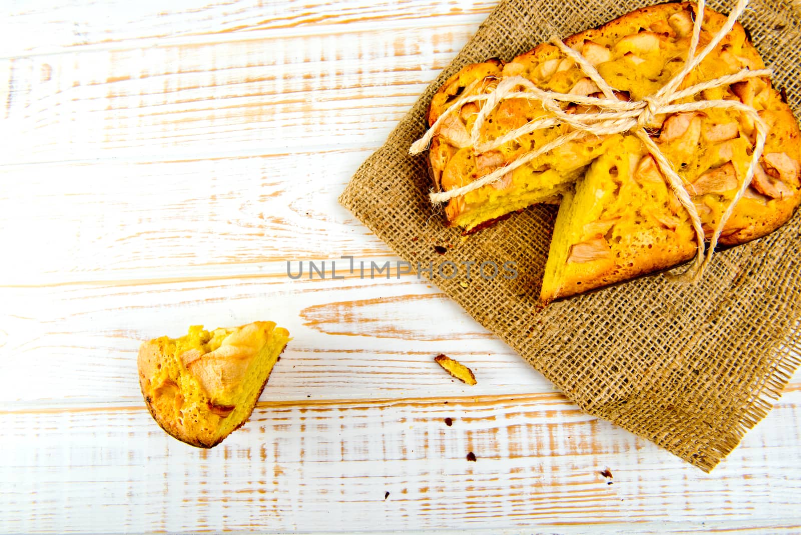 Fresh bakery. Top view of baked pie with apples on sackcloth on a white wooden background. Rustic style.