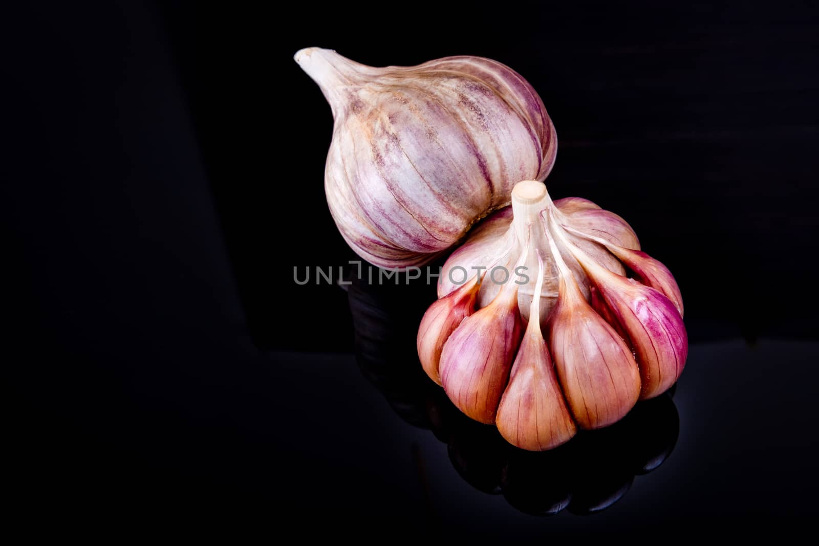 Two heads of garlic on a black background with reflection.