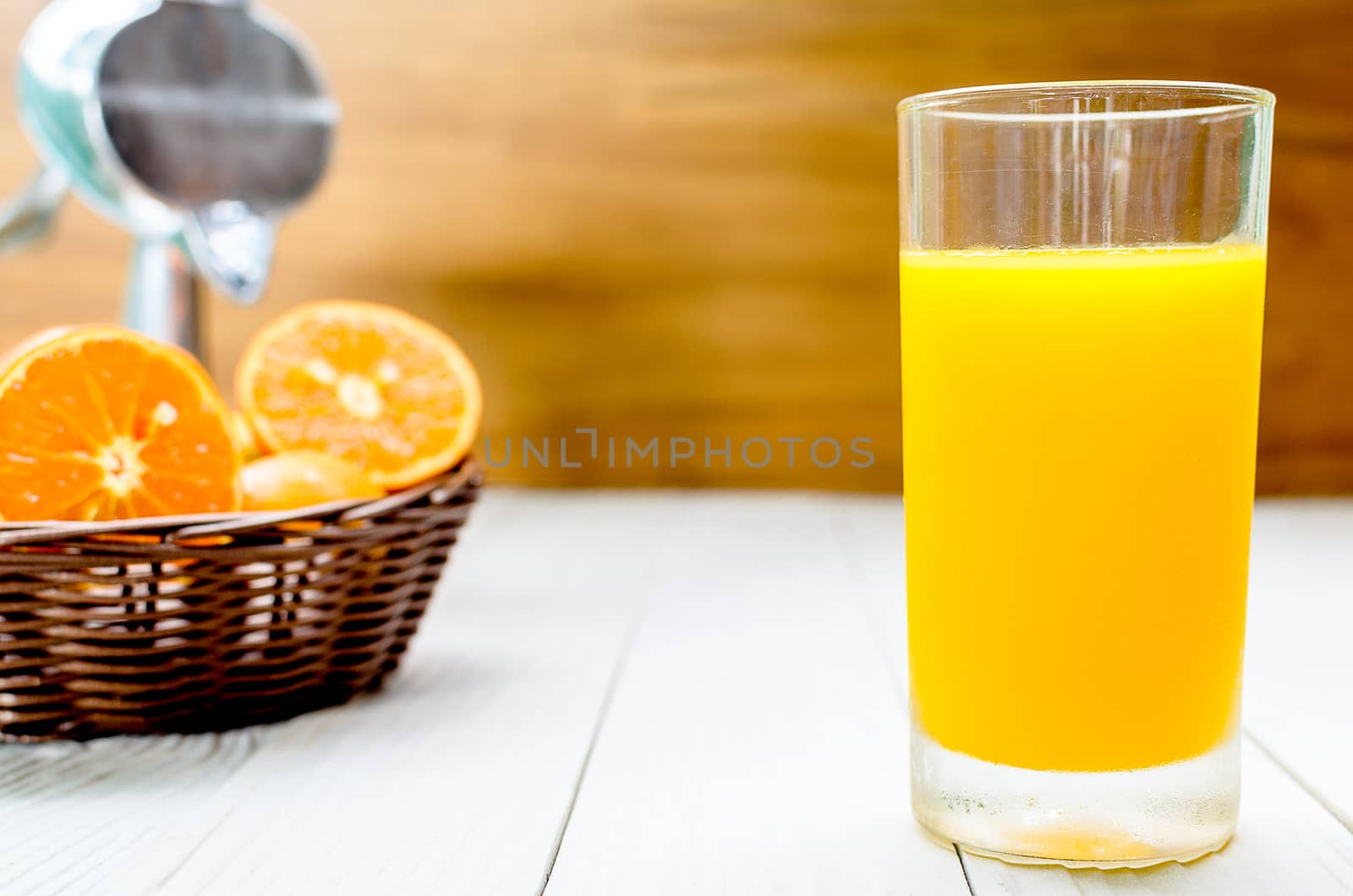 The Freshly Squeezed Orange juice on the white wood table and in front of sliced oranges in the wicker brown basket.