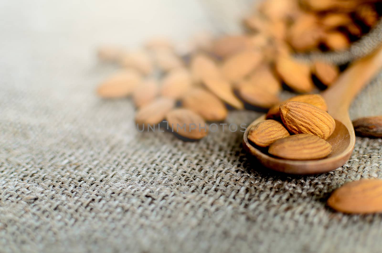 A lot of almonds has putting on the wood spoon and brown napkin.