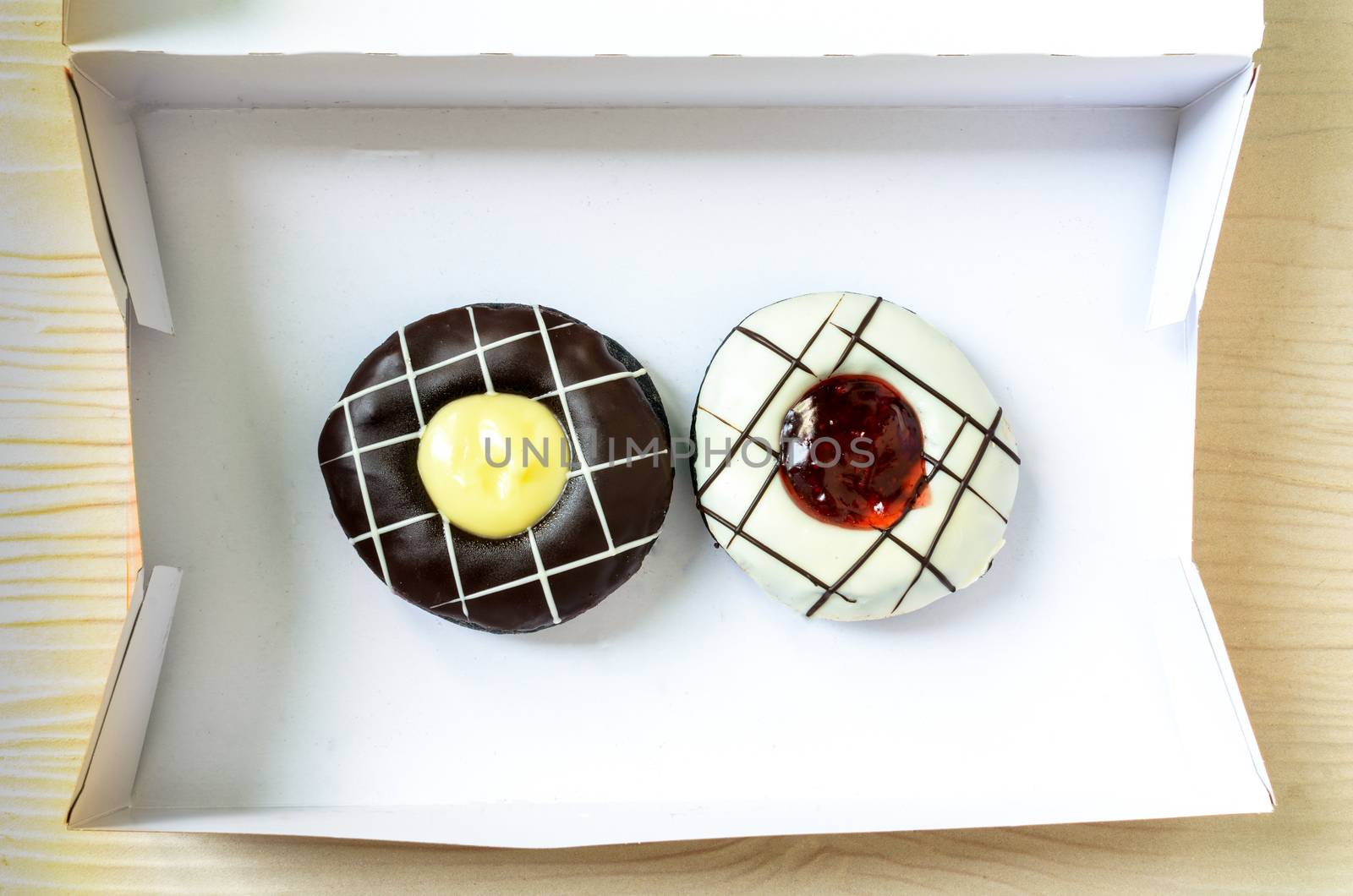 Color donuts in box on the white wood table from top view.