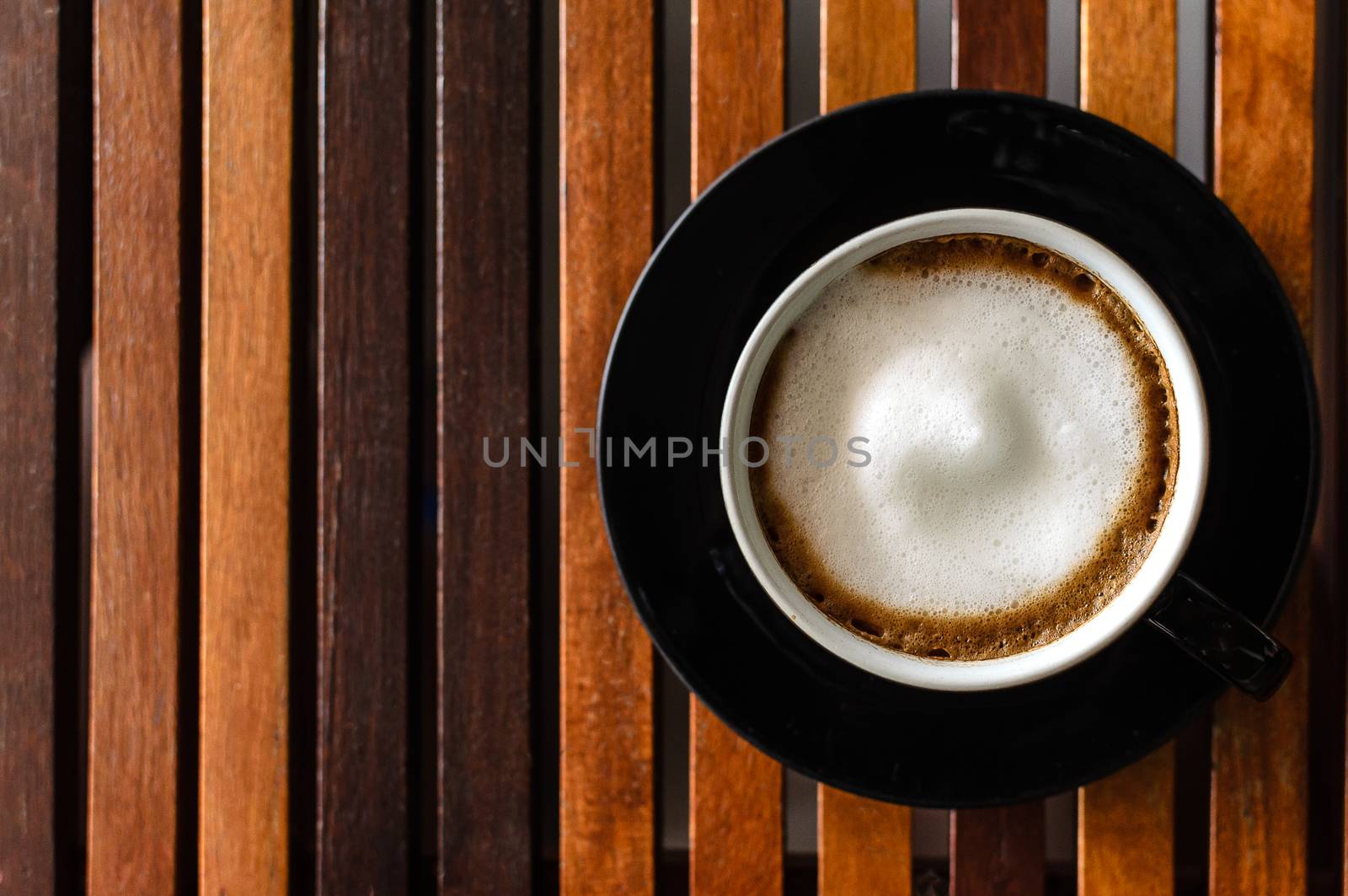 A Cup of Cappuccino Coffee on the horaizontal line brown wood table and ready to served and enjoy drink in the relaxing time with copy space.