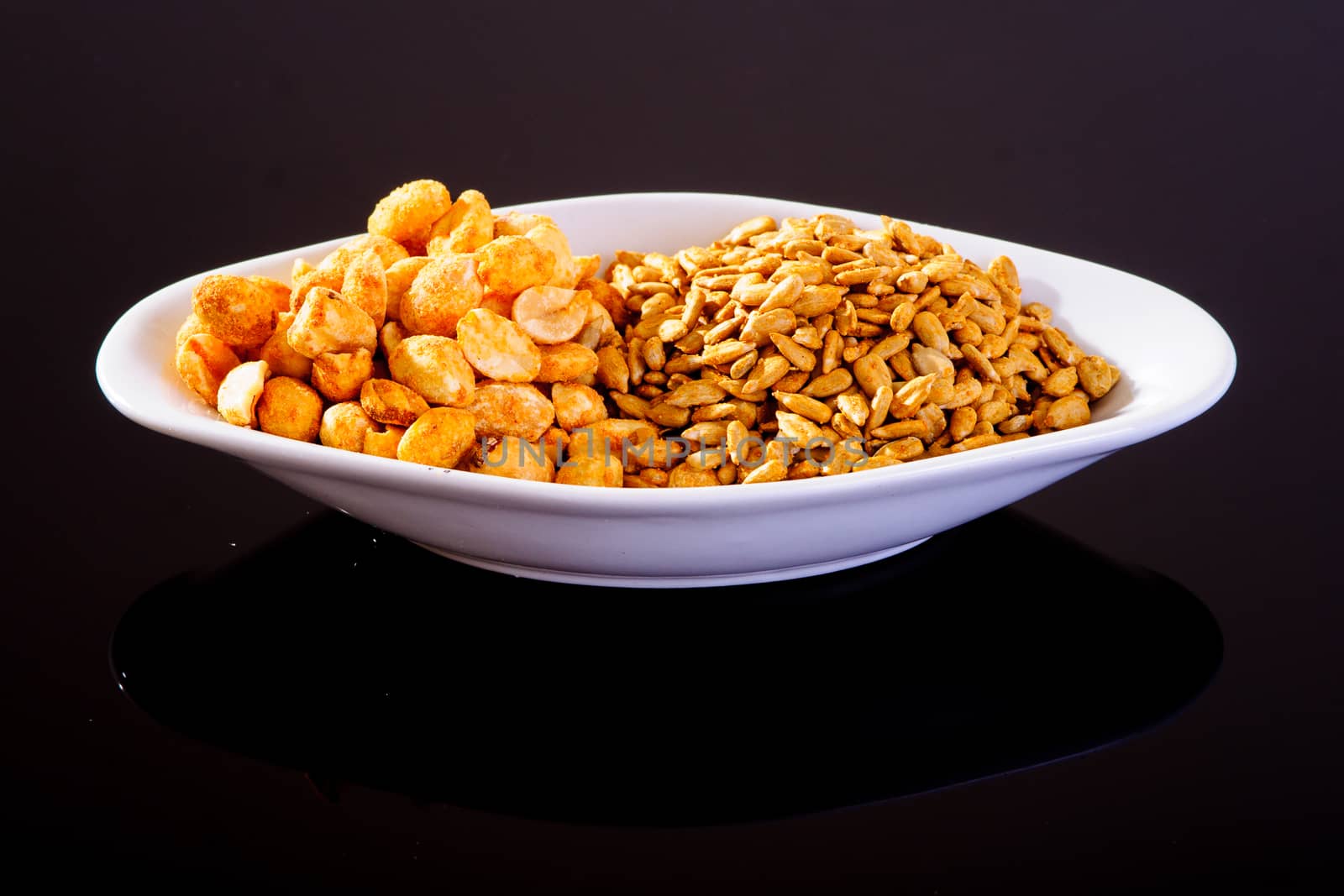 Pumpkin Seeds and Roasted Salted Peanuts in a white plate on a black background