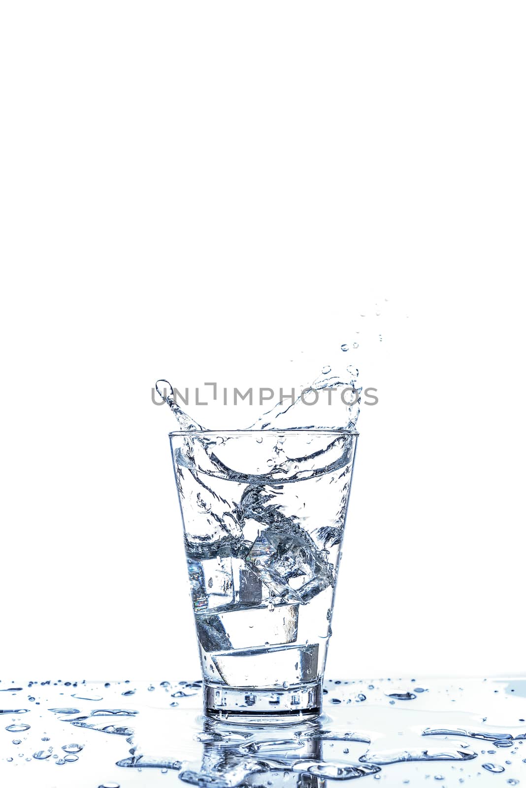 Ice dropping and water splashing in the glass with reflection on the mirror table and isolated on white background.