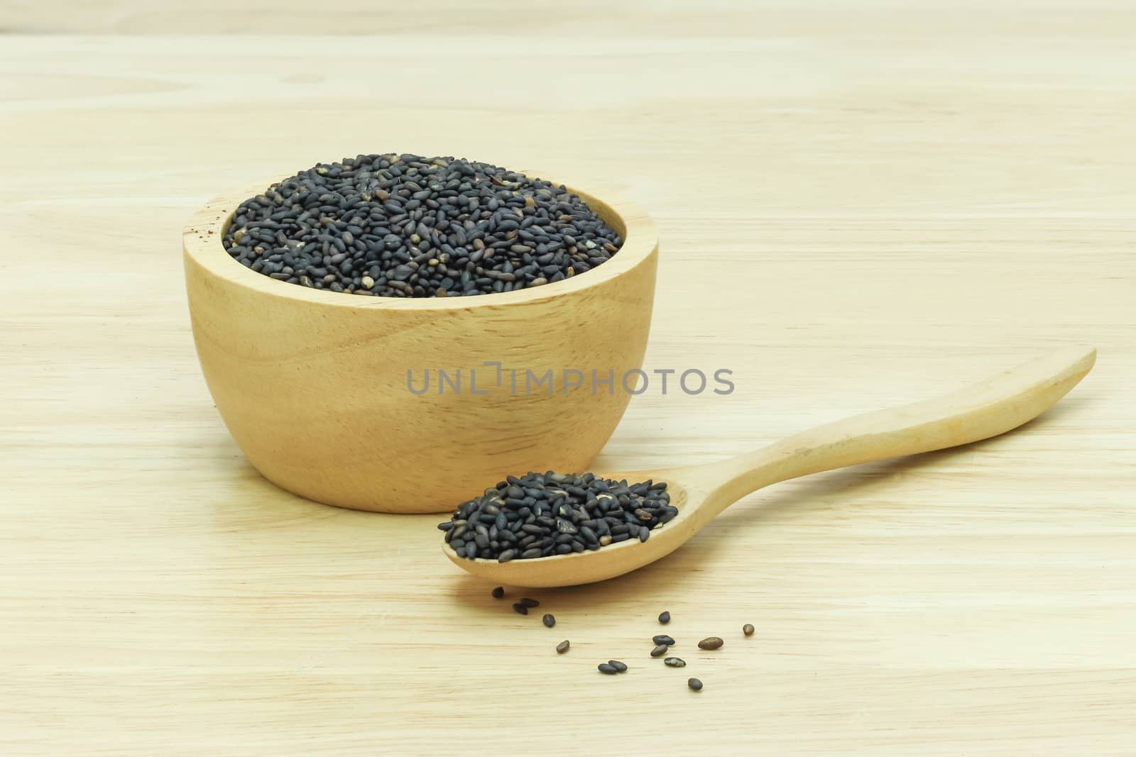Black sesame seeds in wooden spoon pile on wood table 