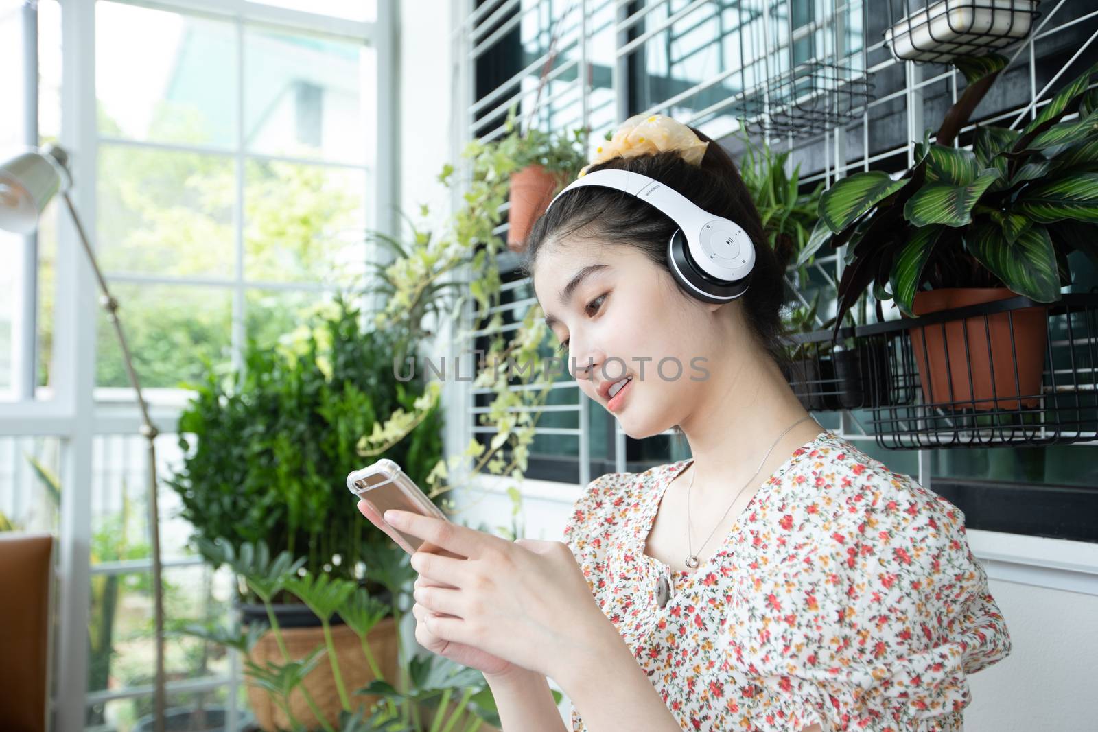 Asian women wearing headphones and using mobile phone and digital tablet for Listening to music and singing on a relaxing day at home by Tuiphotoengineer