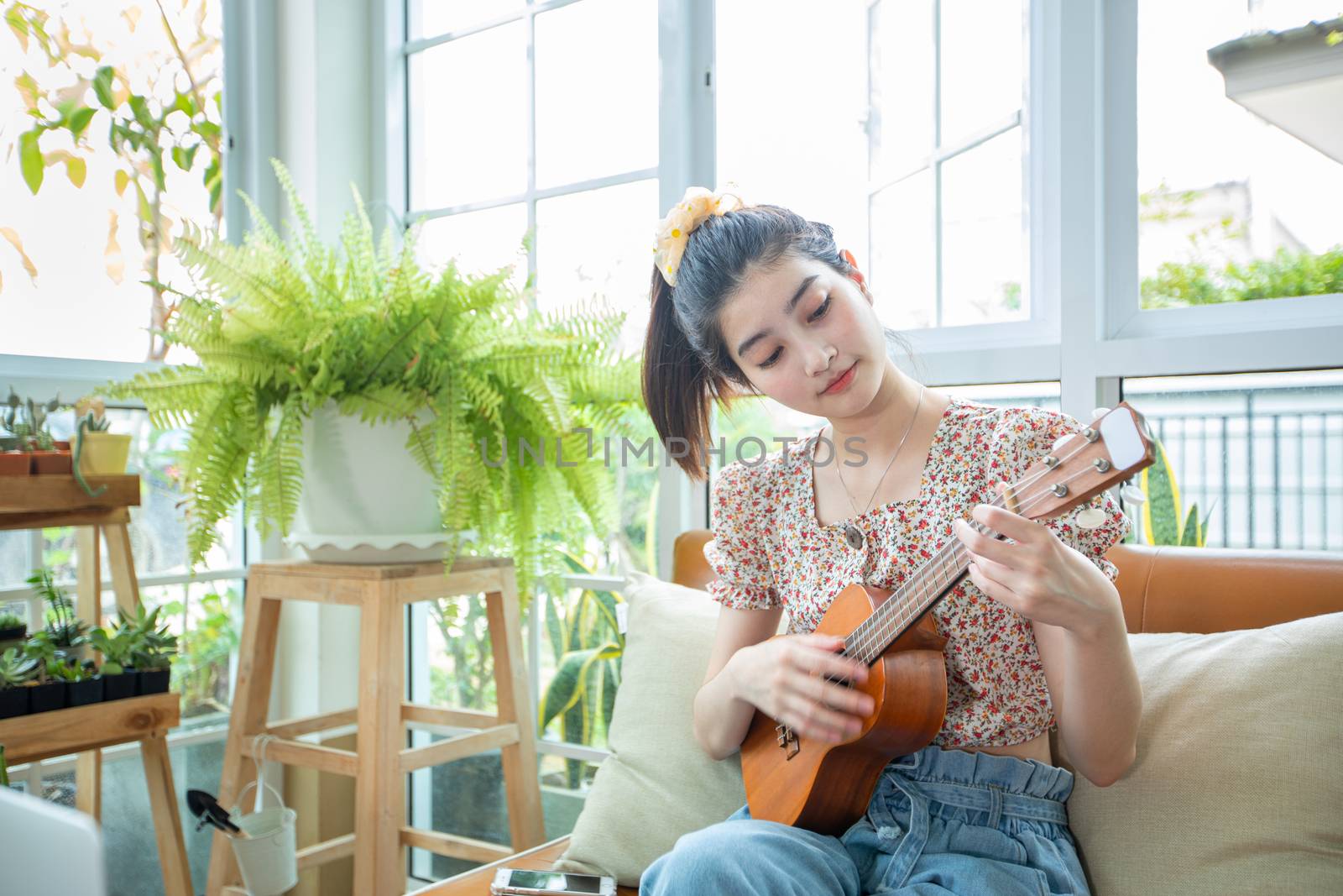 Asian women use their notebook computers to study and practice playing ukulele on the internet at home.