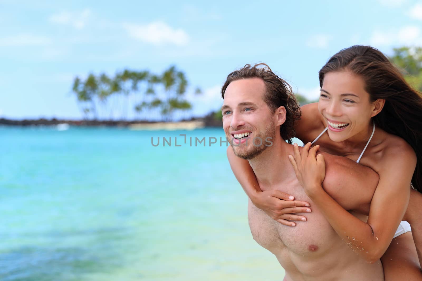 Beautiful healthy young people having fun. Multiracial piggyback couple on beach travel vacation in Caribbean destination. Happy smiling man piggybacking Asian woman.