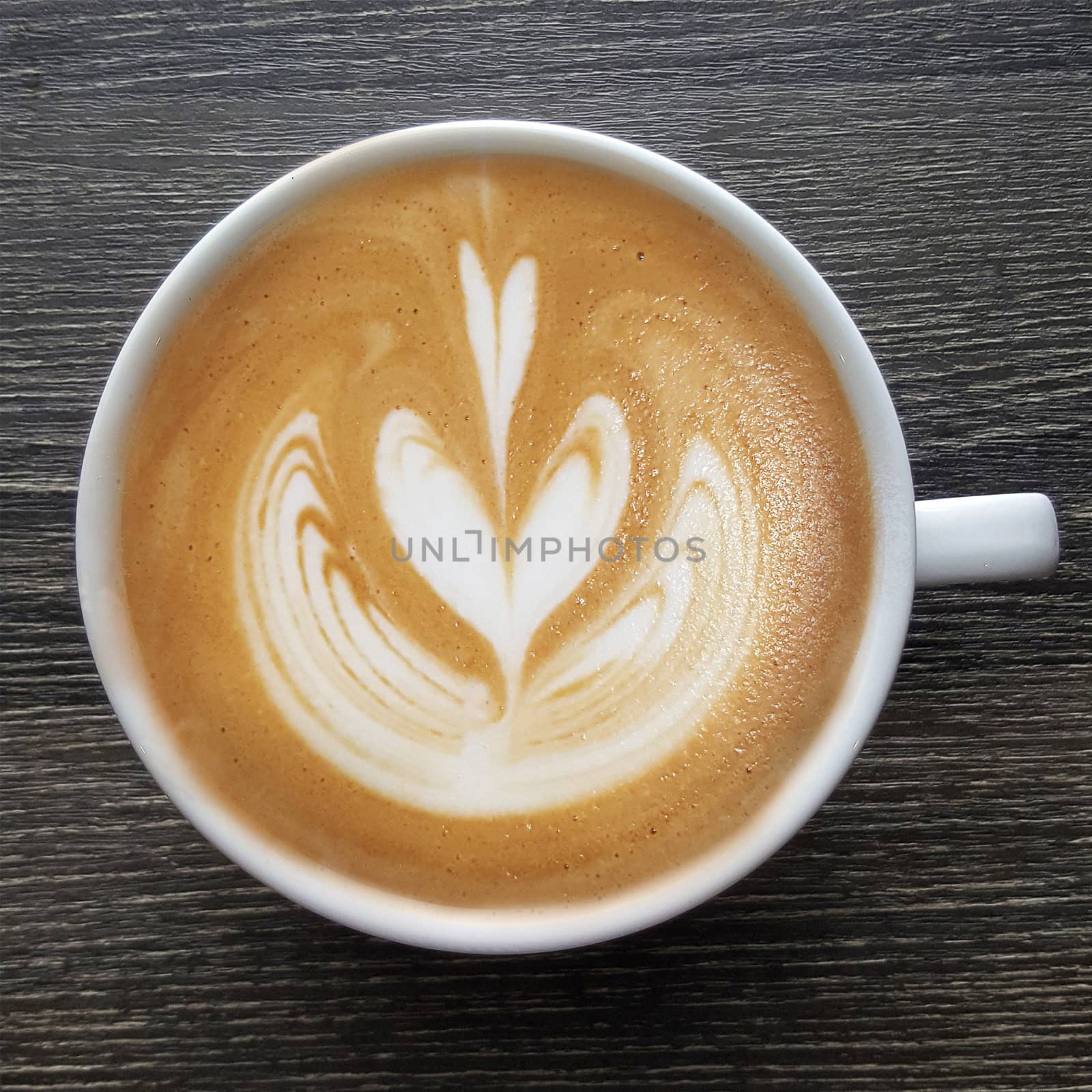 Top view of a mug of latte art coffee on timber background.