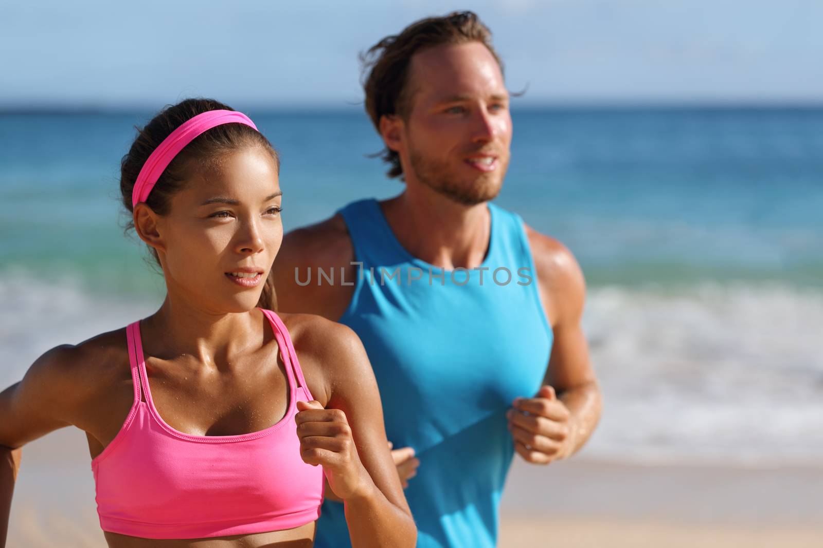 Couple runners running on beach. Interracial young adults asian woman, caucasian man, training cardio together doing outdoor workout jogging by Maridav