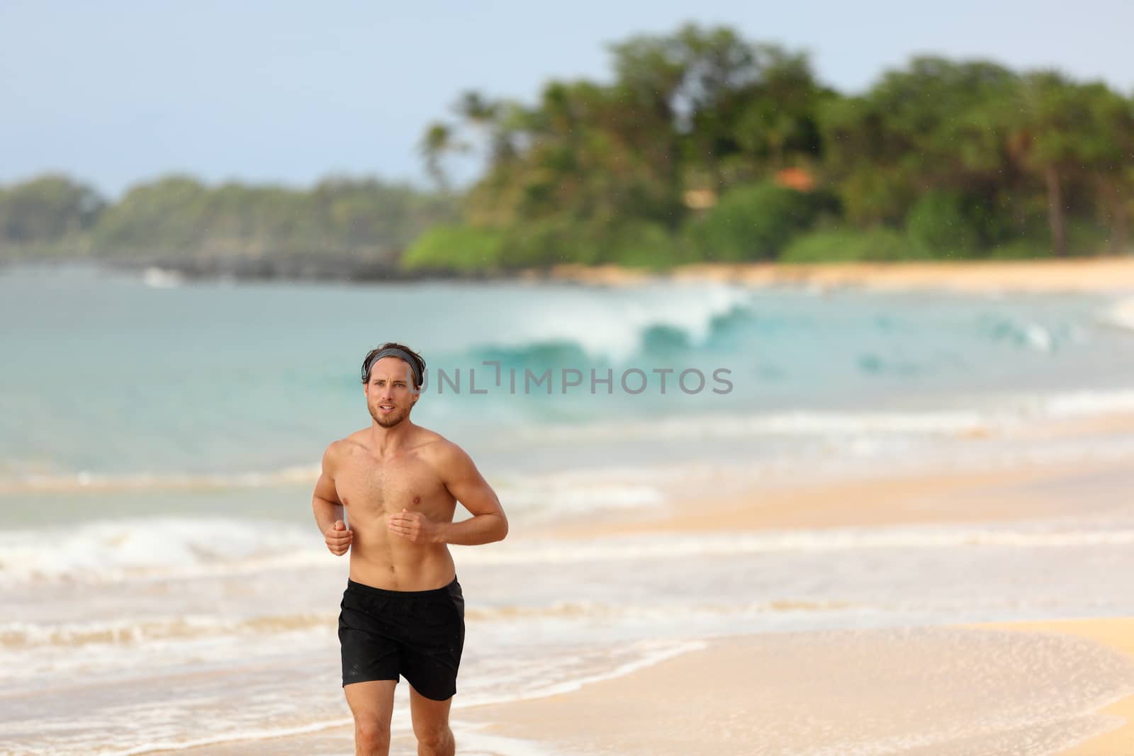 Man athlete running topless in shorts on beach at sunset. Male runner training cardio alone doing exercise on sand with ocean background. Healthy active lifestyle.