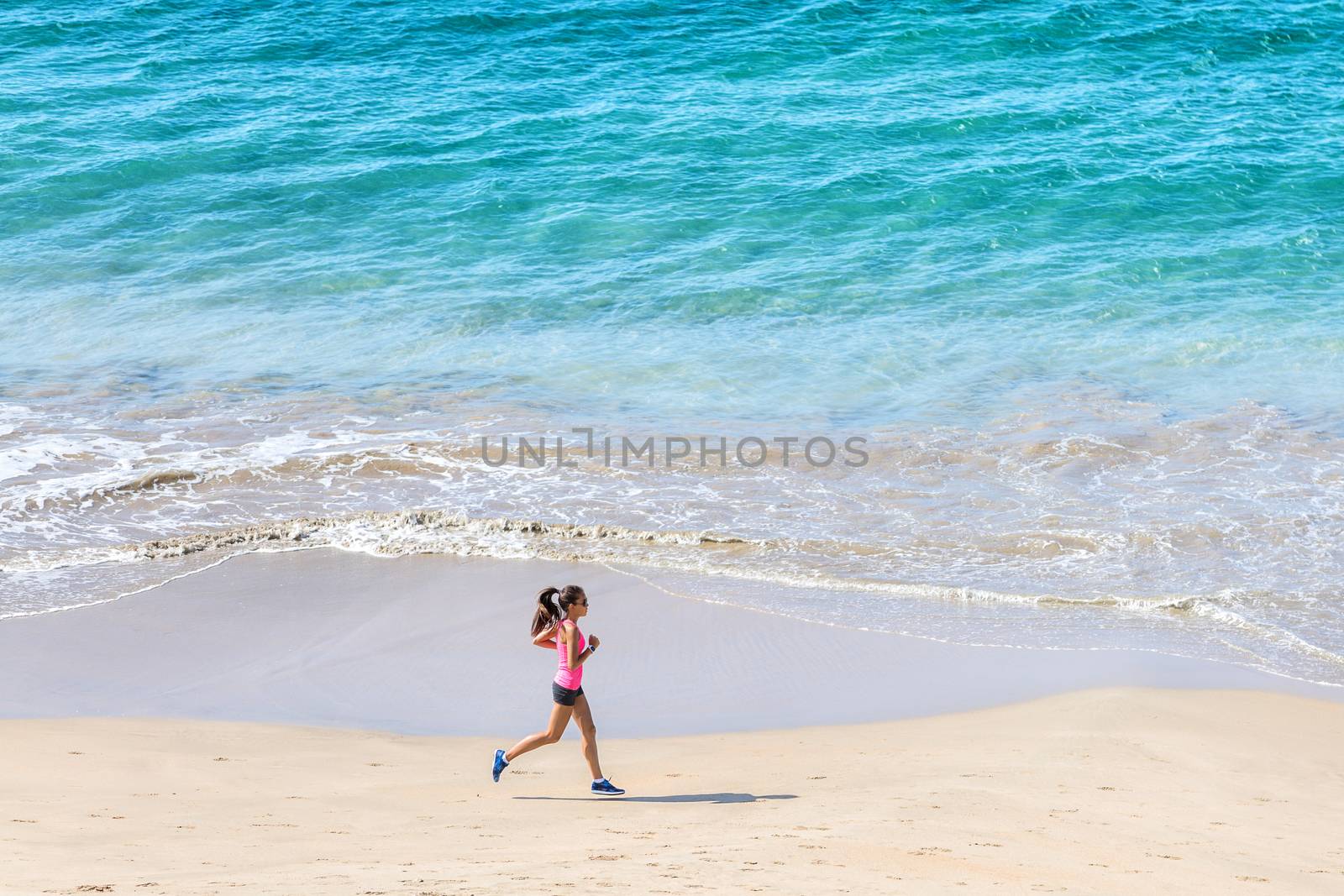 Woman runner training cardio running by the ocean on the beach. Morning workout. Copyspace on blue water.