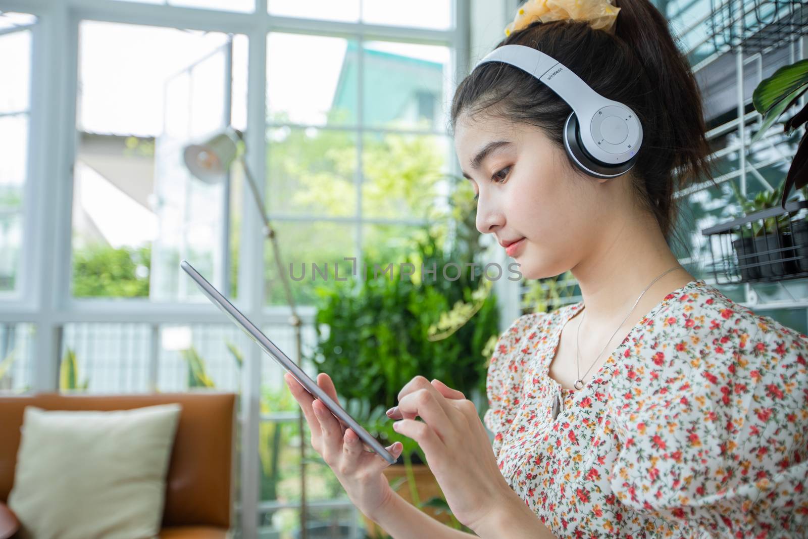 Asian women wearing headphones and using mobile phone and digital tablet for Listening to music and singing on a relaxing day at home by Tuiphotoengineer