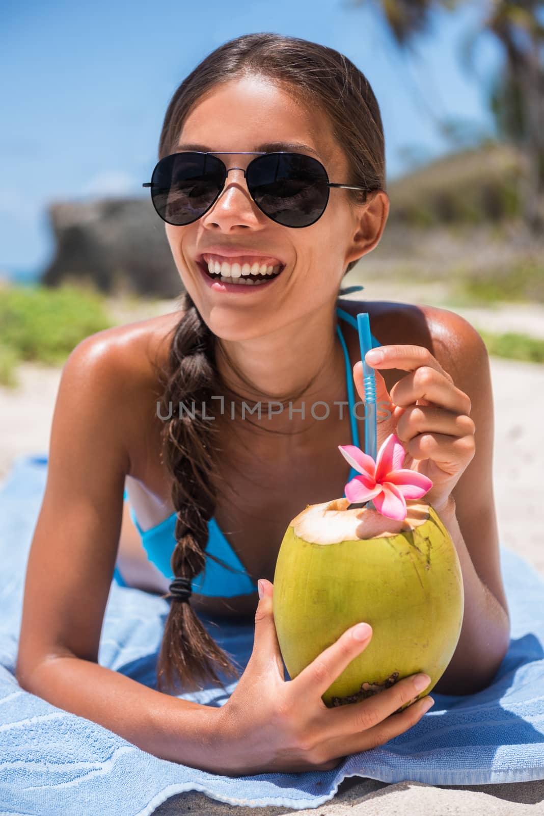 Happy beach girl with sunglasses having fun drinking fresh coconut water on summer vacation. Tropical travel holidays. Sun tanning tourist woman relaxing enjoying drink. Closeup of face by Maridav
