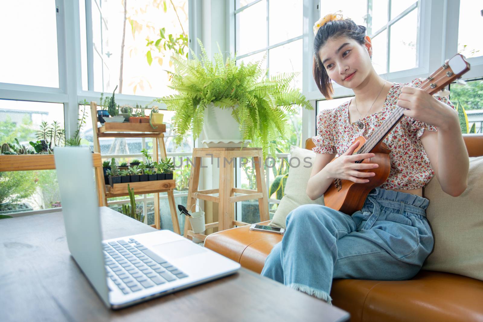 Asian women use their notebook computers to study and practice playing ukulele on the internet at home. by Tuiphotoengineer