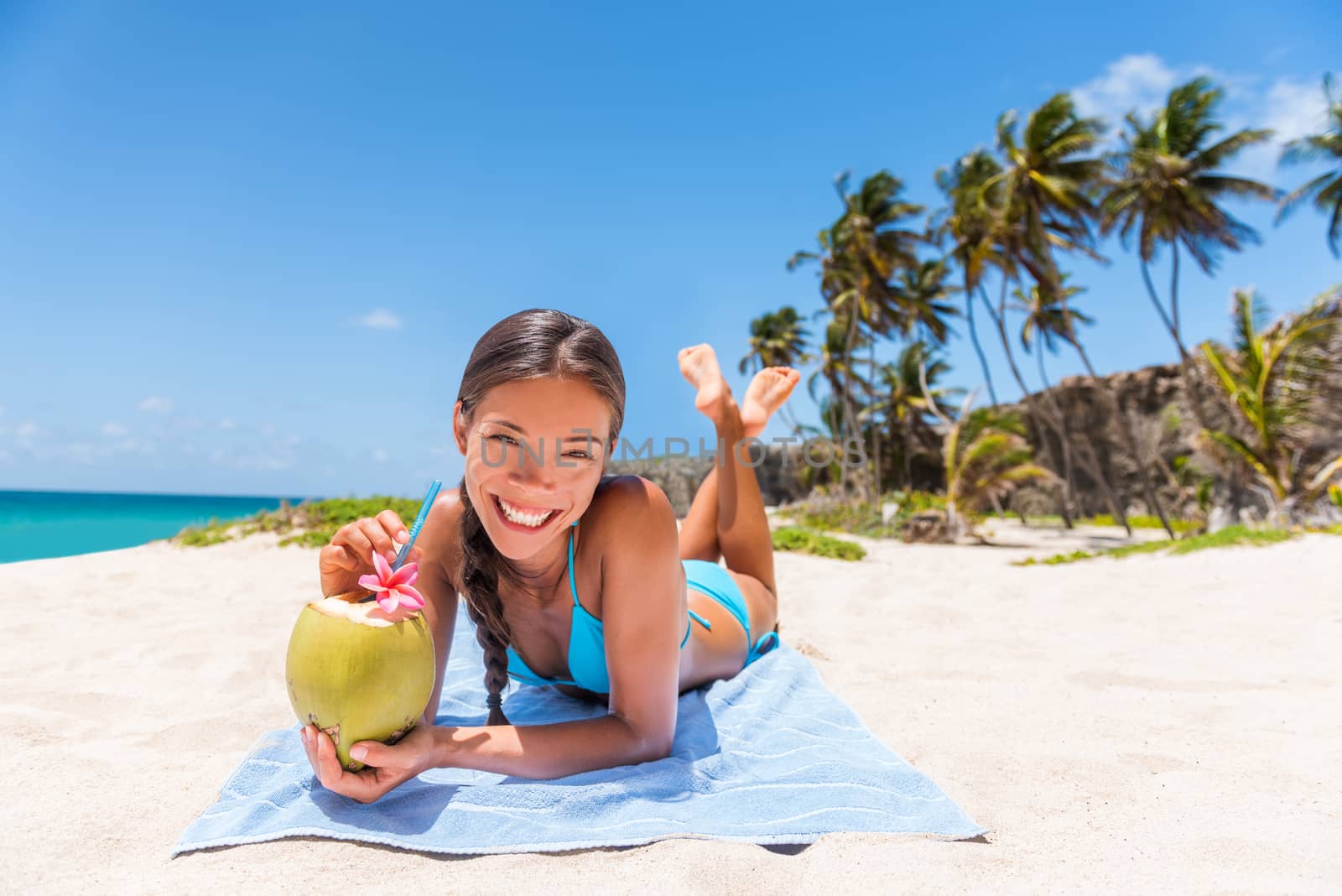 Asian woman relaxing on beach vacation. Happy girl tourist sunbathing drinking healthy organic fresh coconut water. Tropical travel destination, Sun tanning in summer holidays.