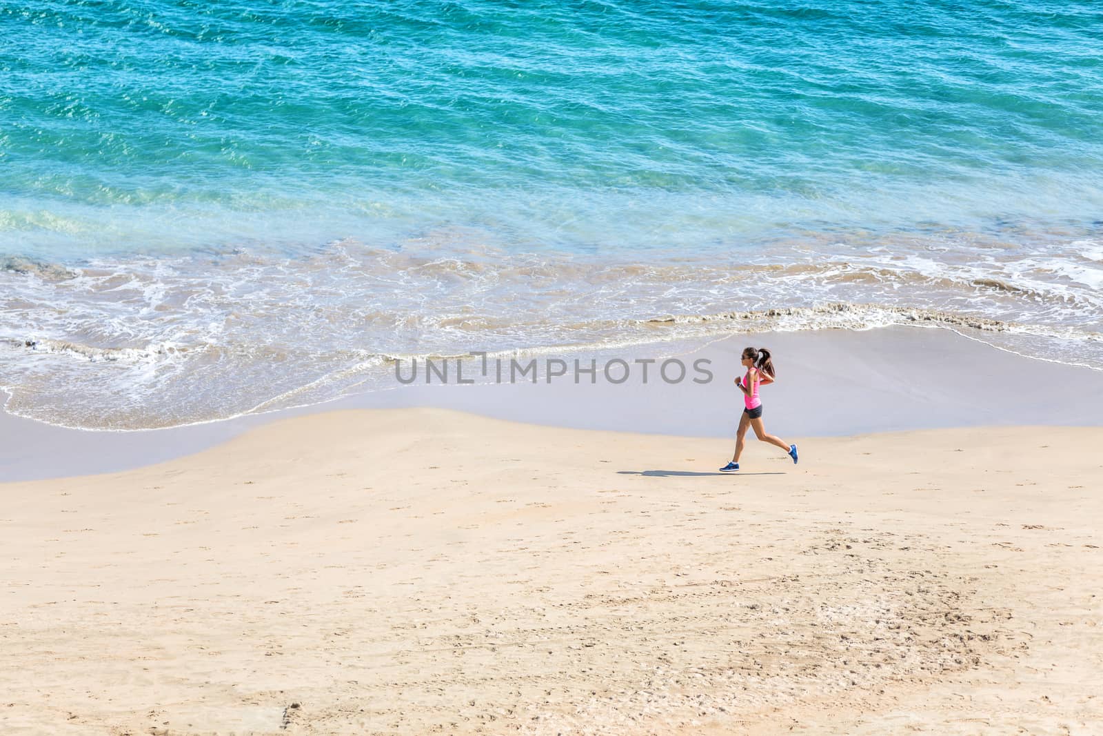 Runner running on beach by the ocean - view from above. Woman athlete training cardio jogging doing morning workout. Hero shot, lots of copyspace.