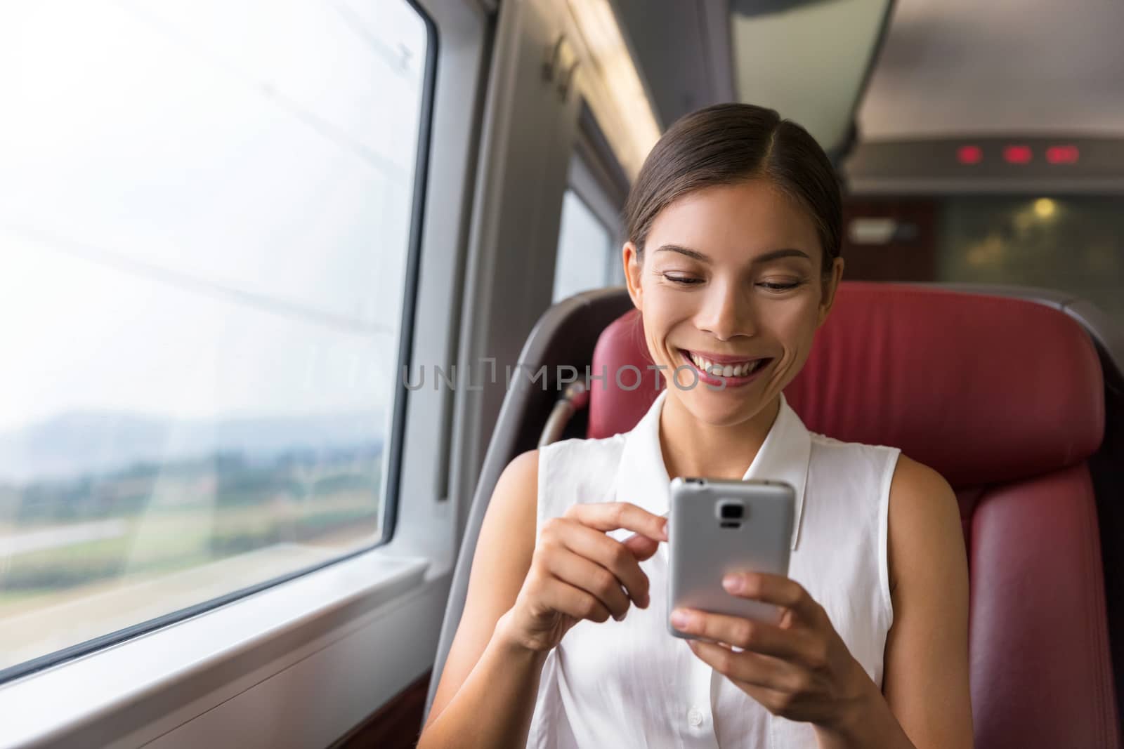 Happy Asian businesswoman using mobile phone app to text sms message or play video games while commuting to work in train. Woman sitting in transport enjoying travel.