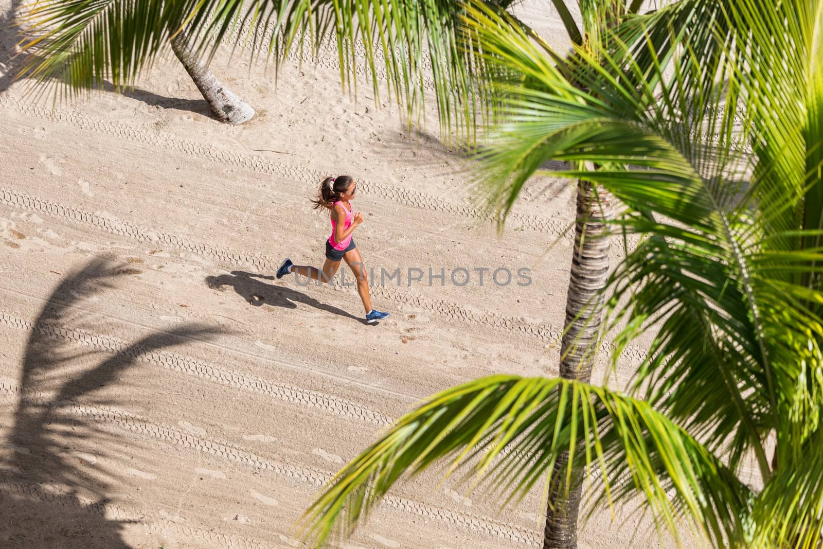 Fitness athlete running training cardio on beach. Woman jogging in between palm trees. View from above of the ground and sand. Health and sports concept. Copyspace.
