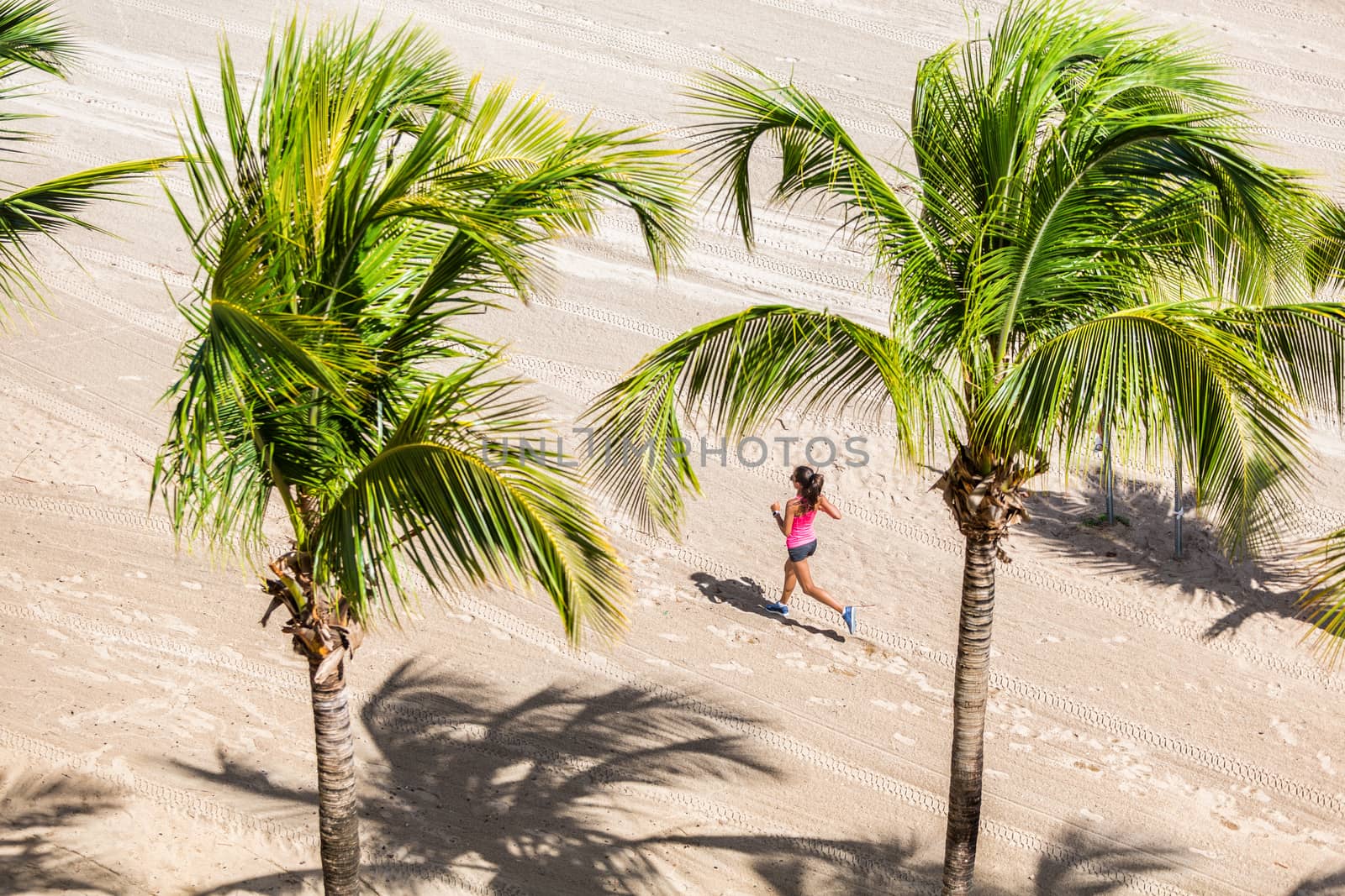 Fitness woman running training on tropical beach in between palm trees. View from high angle, hero shot. Health and sports concept. Copyspace.