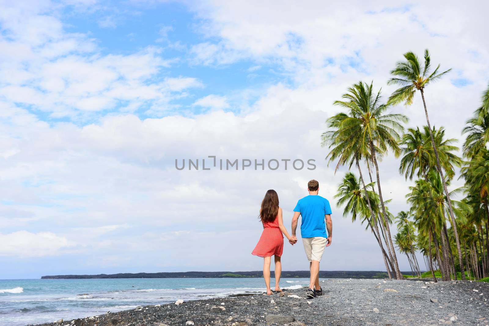 Couple walking on Hawaii secluded black sand volcanic beach on the Big island of Hawaii, hawaiian destination tropical travel for summer vacations. People from behind relaxing on walk by Maridav
