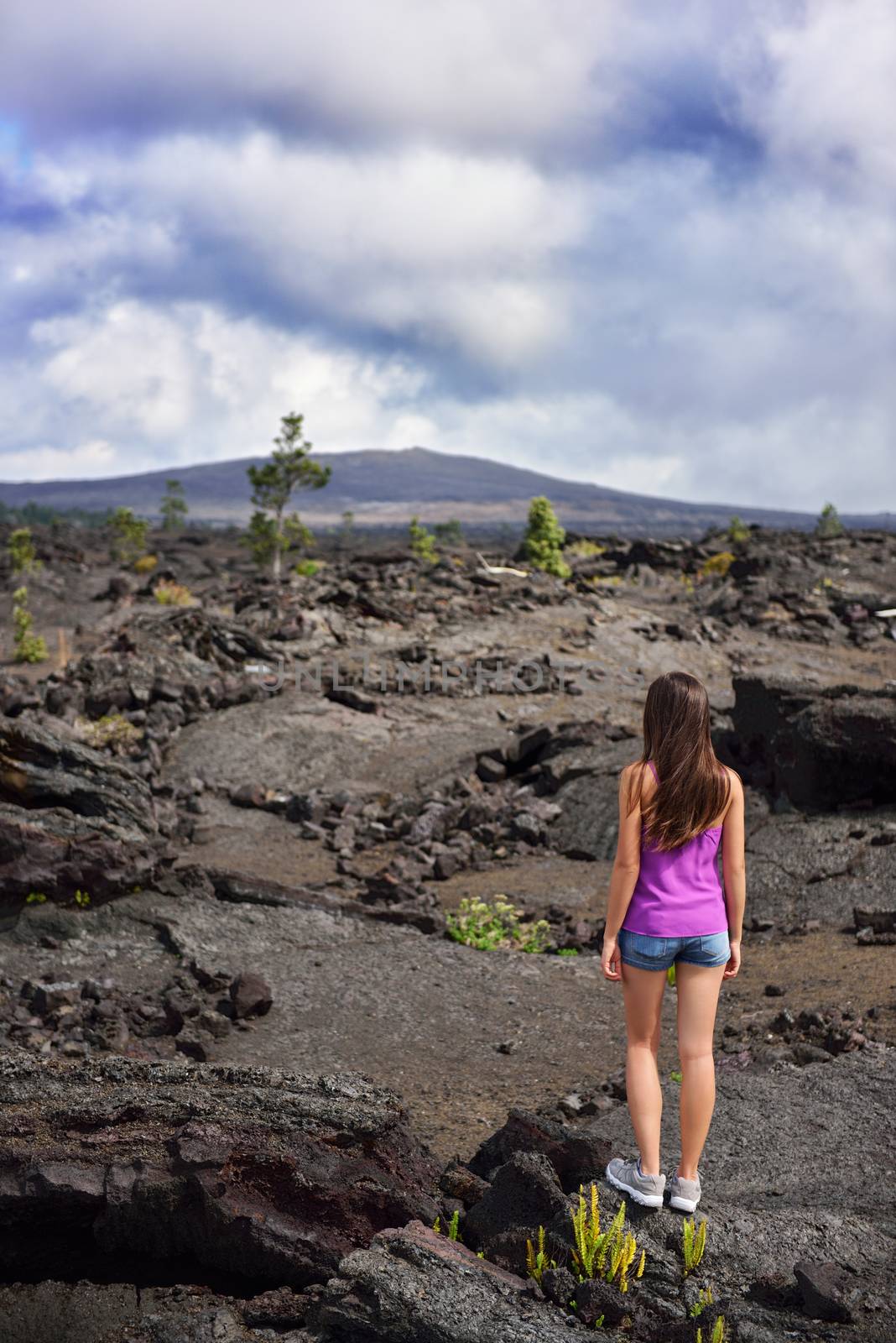 Woman hiking in volcanic rocks on volcano of Big island of Hawaii, USA. Tourist hiker walking on volcanic black rocks during summer traveling holidays.