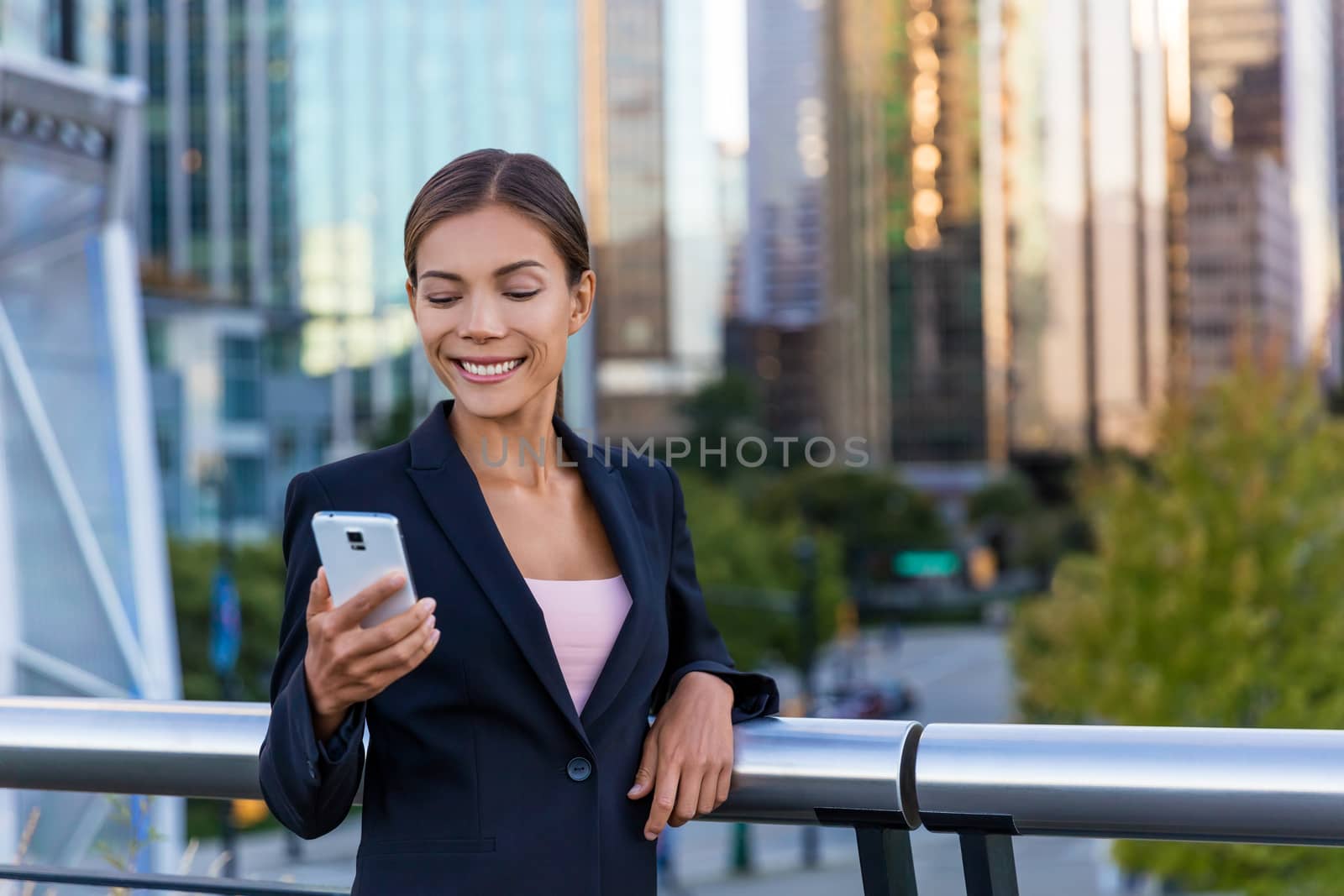 Woman sms texting using app on smart phone in city business district. Young business woman using smartphone smiling happy wearing suit jacket outdoors. Urban female professional in her 20s.