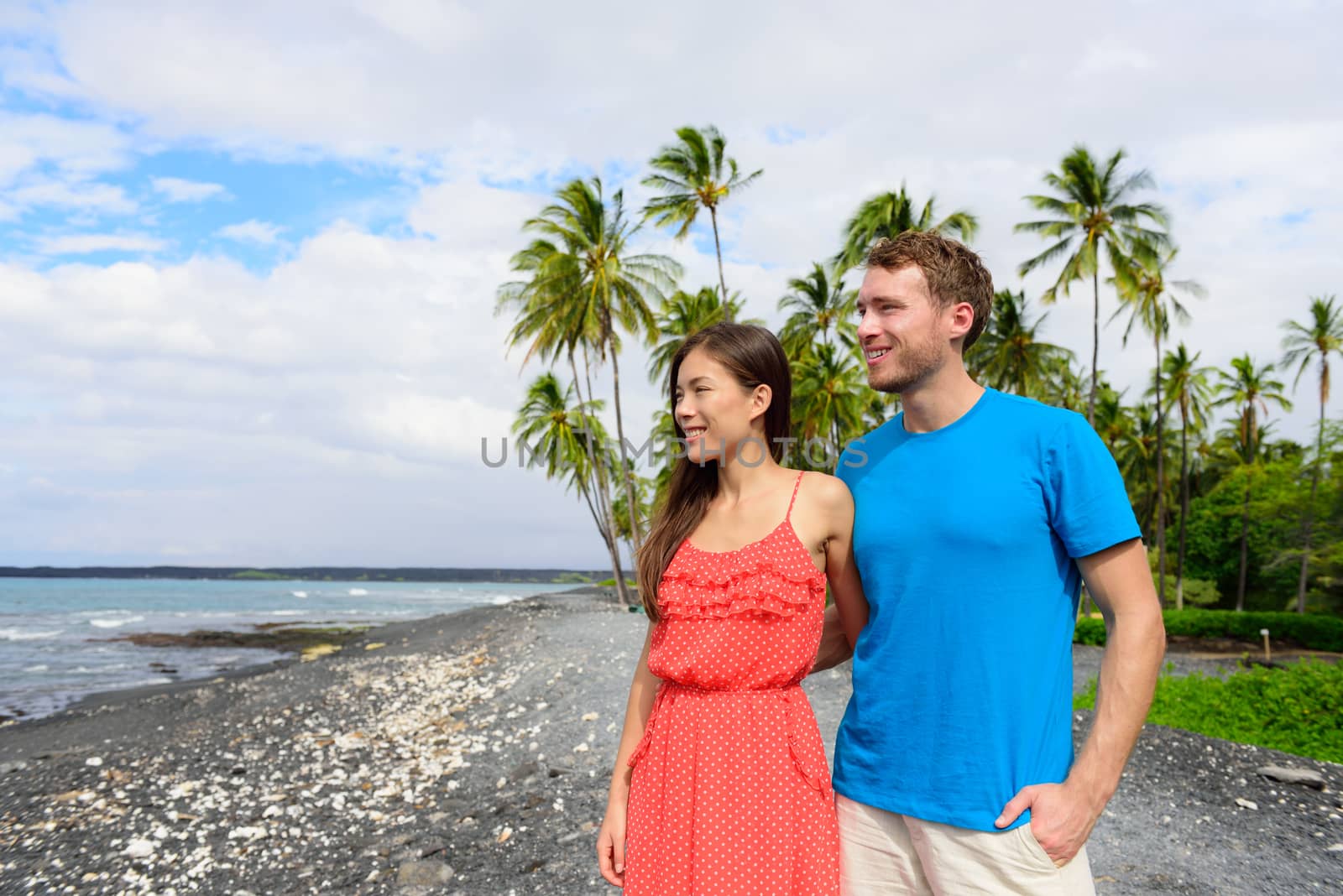 Hawaii couple enjoying beach holidays looking at view of ocean from black sand volcanic beach on Big Island of Hawaii, hawaiian travel vacation.