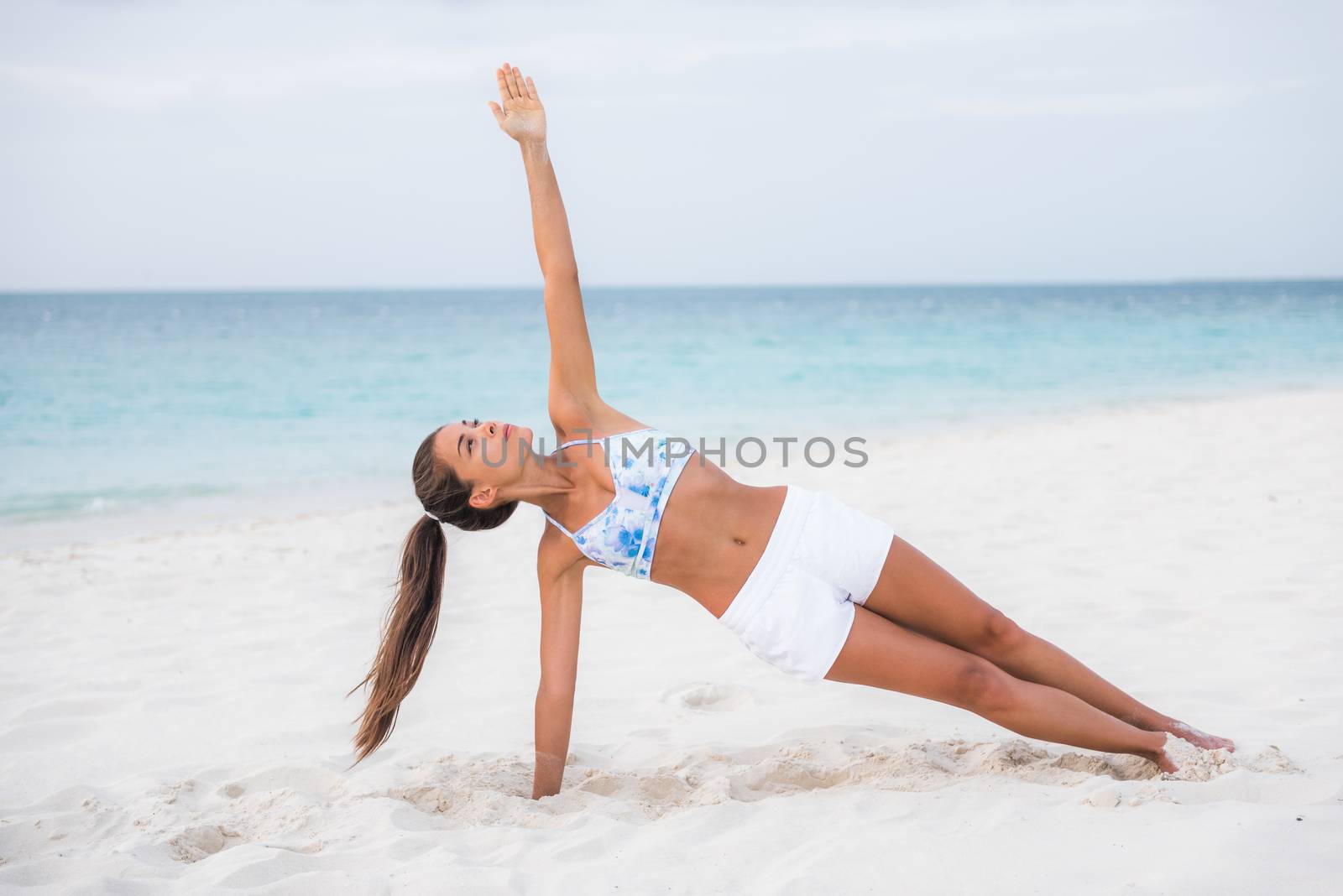 Side plank yoga fitness girl training balance strengthening abs muscles and wrist, toning body with core workout training outside on beach. Asian woman doing bodyweight exercise.