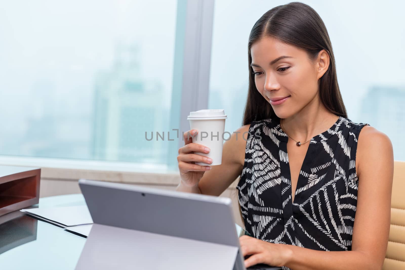 Portrait of a serious businesswoman using laptop at office desk while drinking a coffee cup. Asian woman working on computer at home.