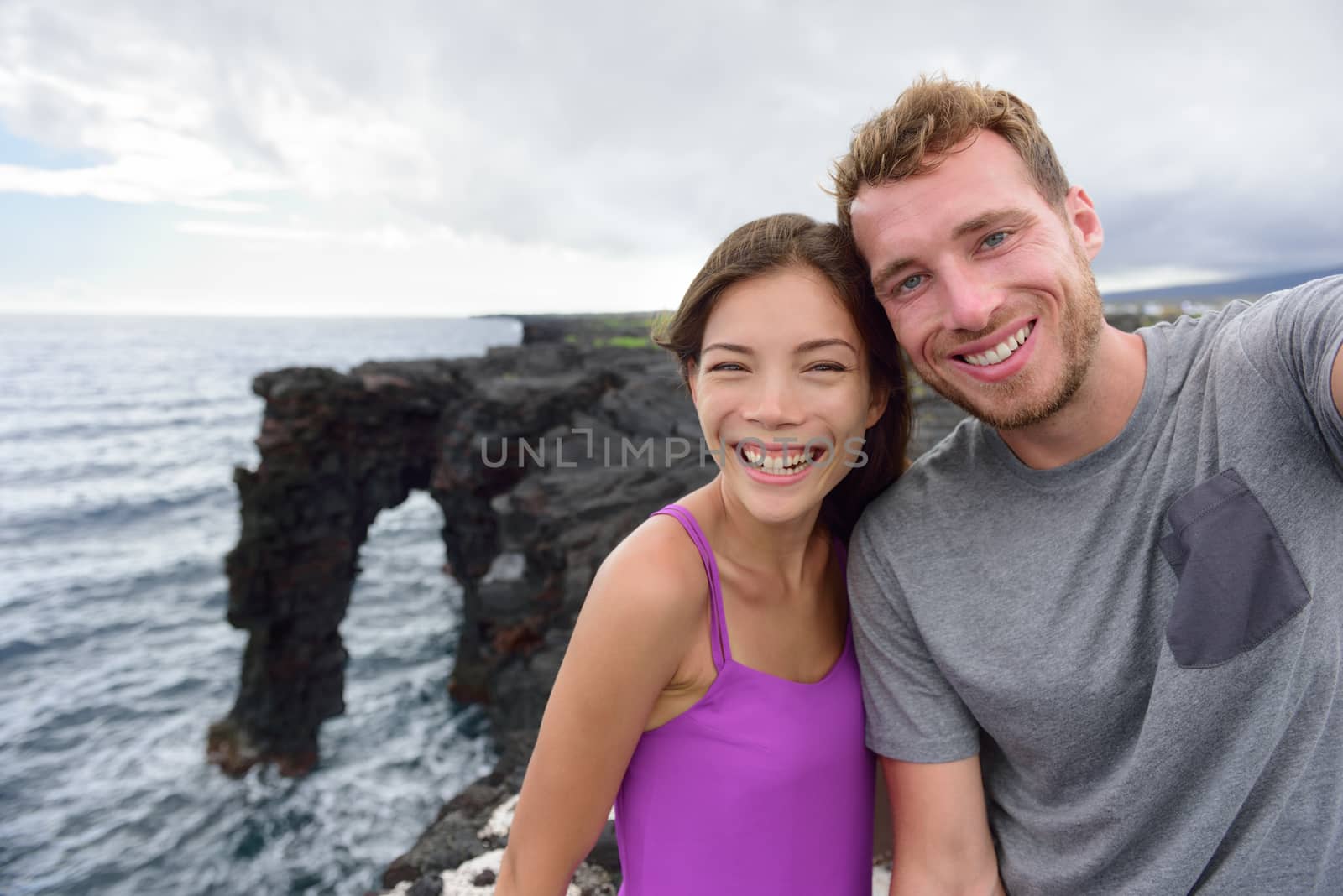 Selfie couple on nature travel Hawaii vacation. Young people taking phone picture at the Holei Sea Arch, tourist attraction on Big Island at the Volcanoes National park by Maridav